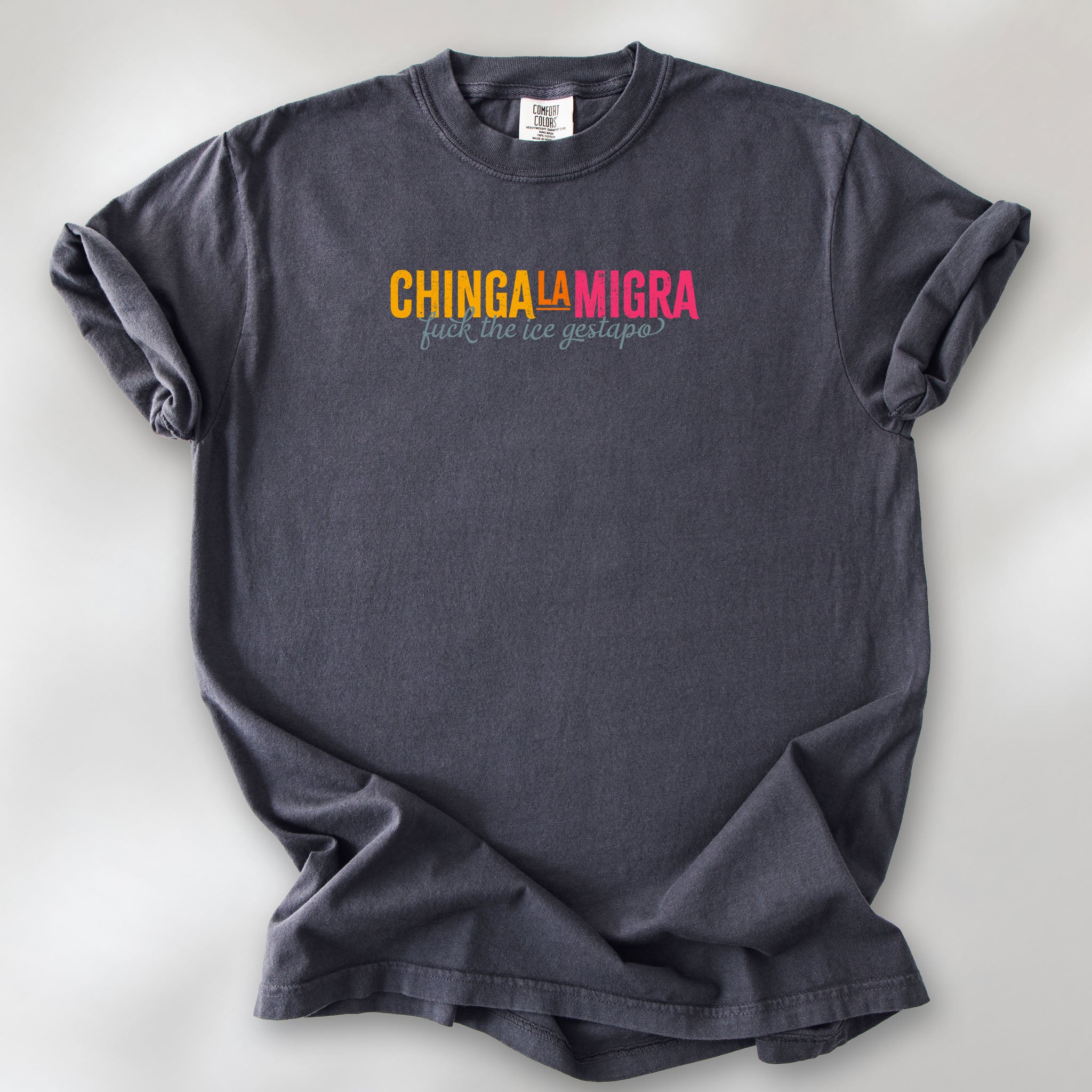 Graphite t-shirt with brightly colored text that reads "chinga la migra", with subtle script text below that says "fuck the ice gestapo."