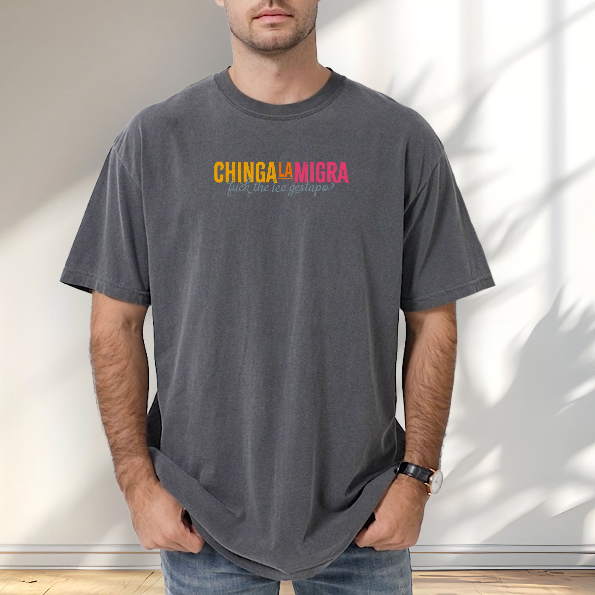 Male mode wearing grey t-shirt with brightly colored text that reads "chinga la migra", with subtle script text below that says "fuck the ice gestapo."