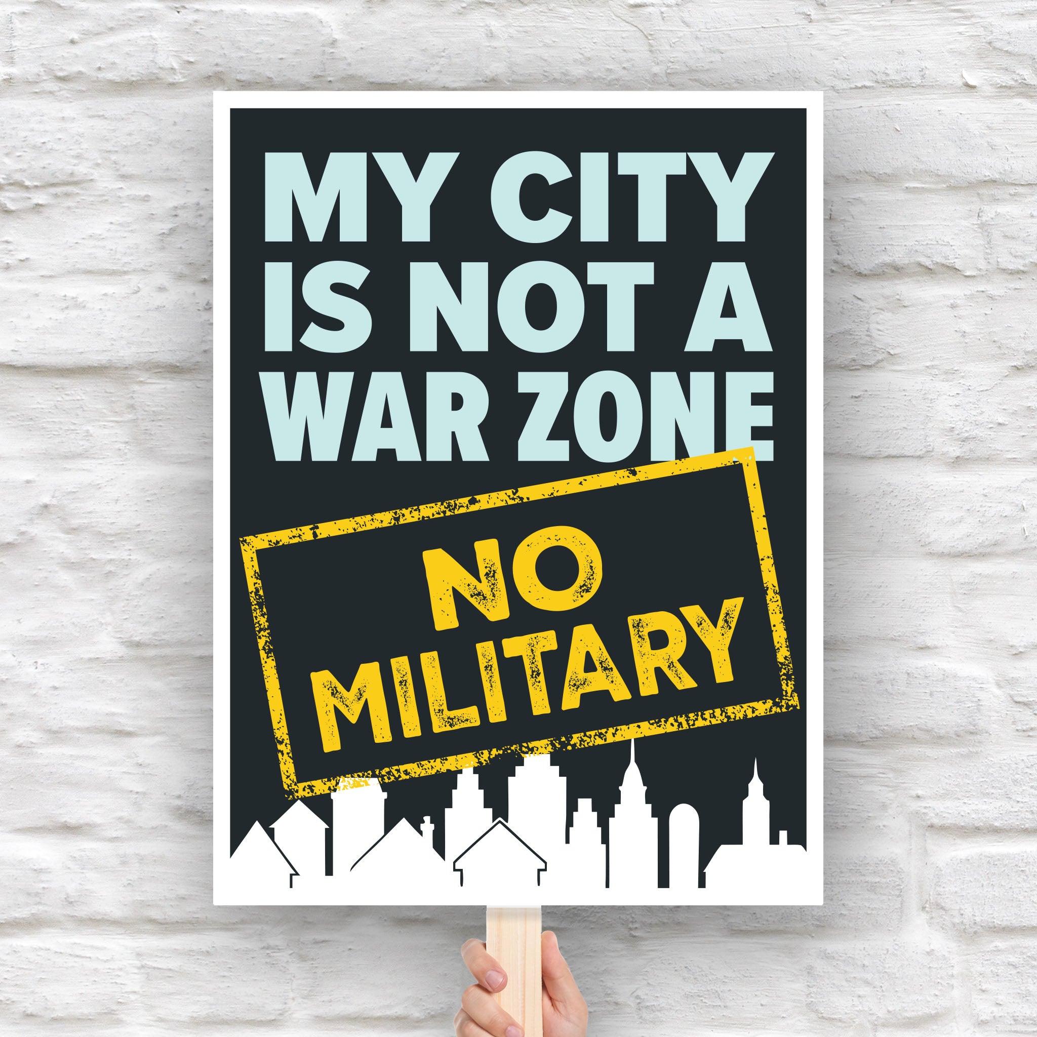Protest sign that reads "My City Is Not a War Zone – No Military" with bold lettering and a city skyline silhouette, anti-Trump political art.