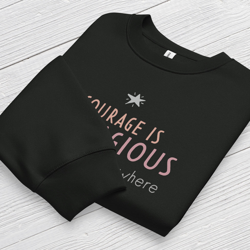 Black crewneck sweatshirt with minimalist stylized text that reads "courage is contagious – spread it everywhere" folded showing neck and sleeve cuff.