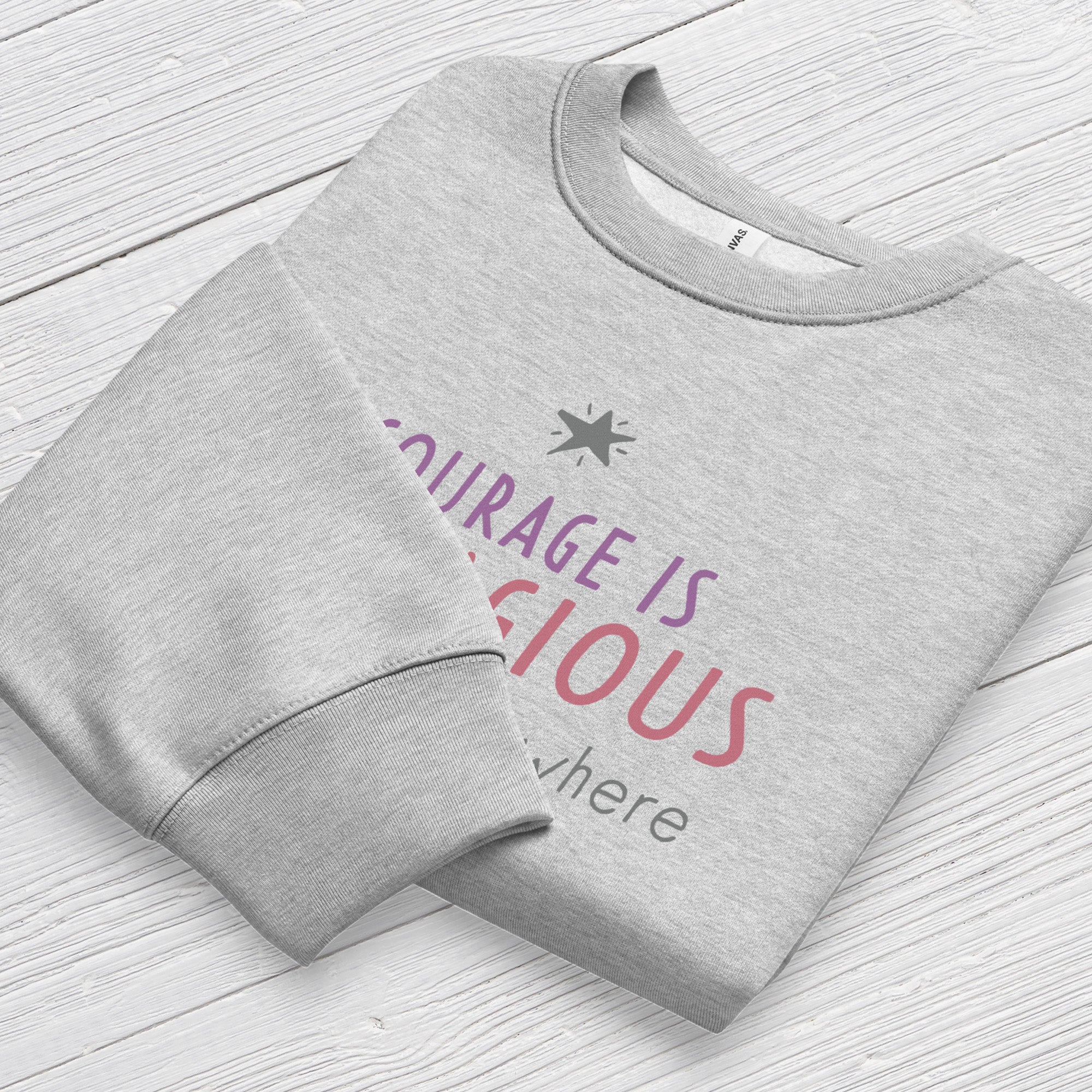 Athletic heather grey crewneck sweatshirt with minimalist stylized text that reads "courage is contagious – spread it everywhere" folded showing neck and sleeve cuff.