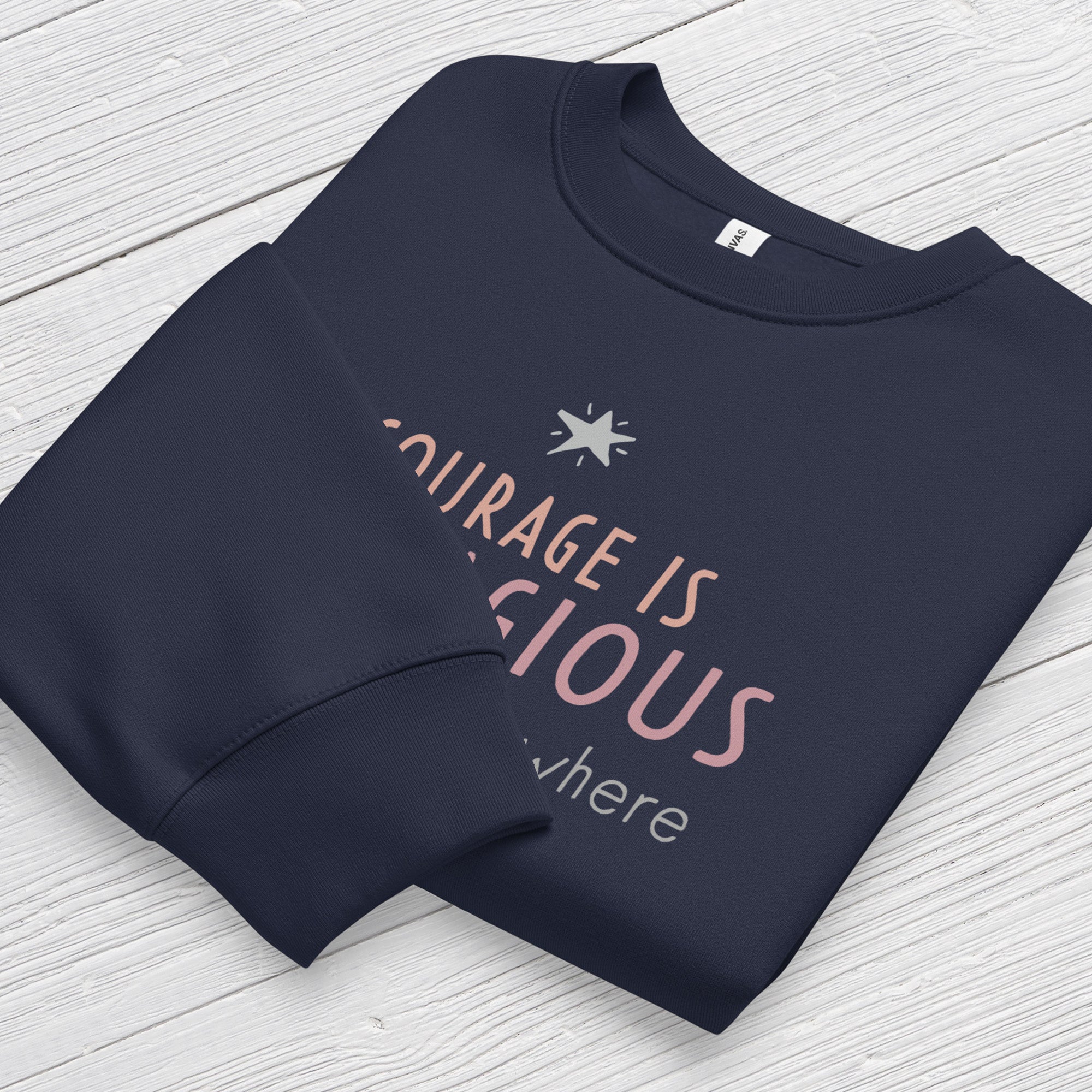 Navy crewneck sweatshirt with minimalist stylized text that reads "courage is contagious – spread it everywhere" folded showing neck and sleeve cuff.