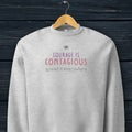 Athletic heather grey crewneck sweatshirt with minimalist stylized text that reads "courage is contagious – spread it everywhere" hanging on a hanger.