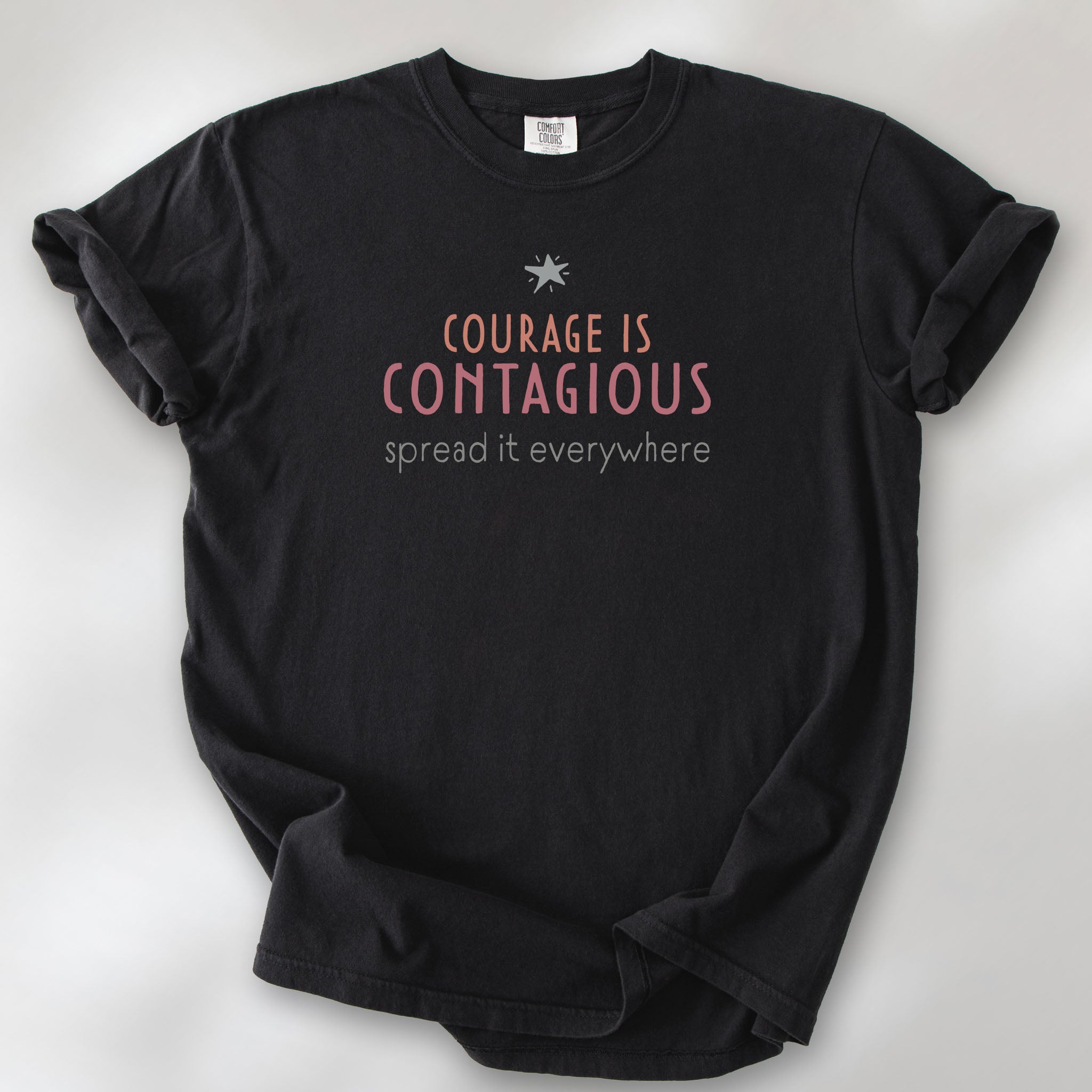 Black t-shirt with the words “Courage Is Contagious – Spread It Everywhere” printed in soft pink, coral, and gray.