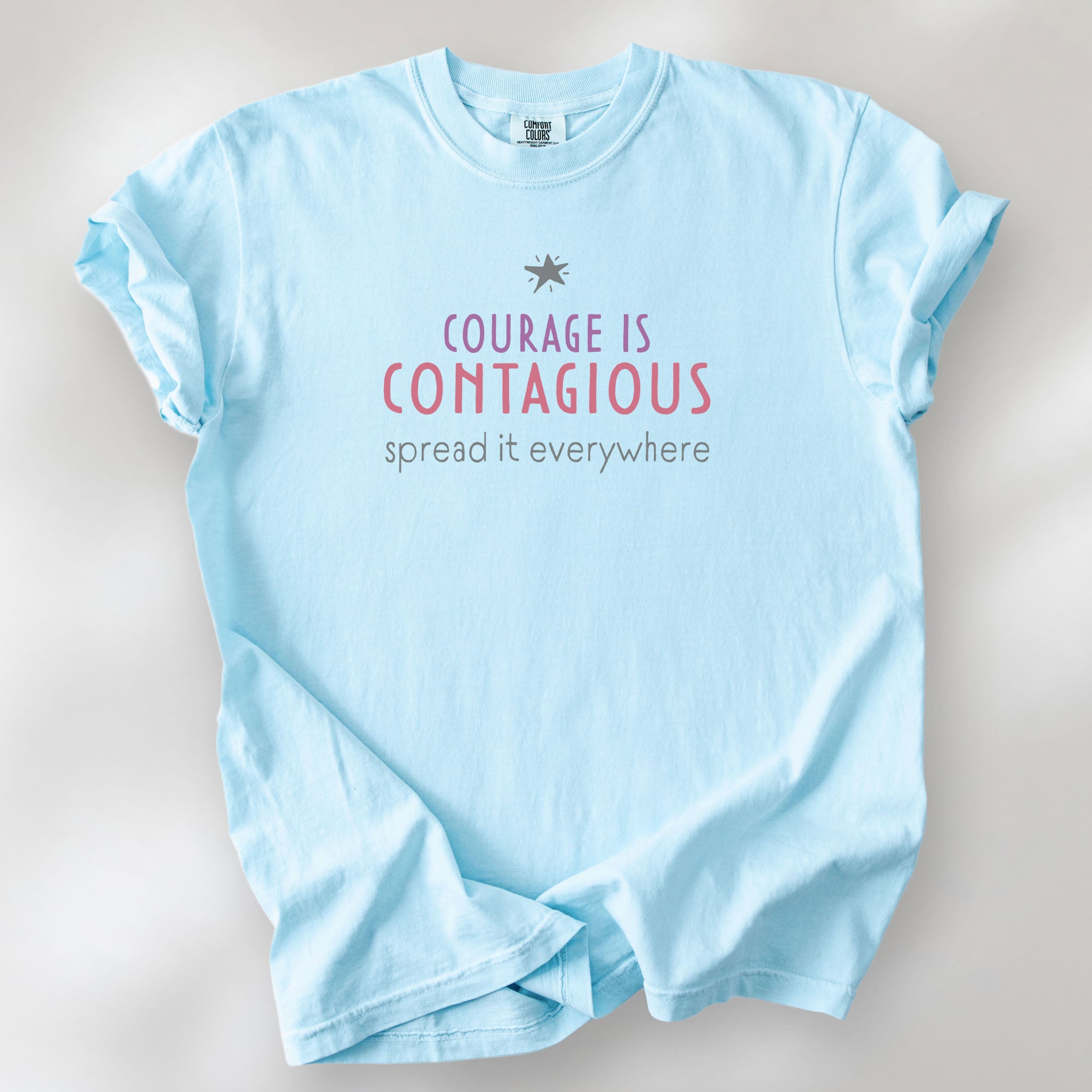 Chambray t-shirt with the words “Courage Is Contagious – Spread It Everywhere” printed in soft purple, red, and gray.
