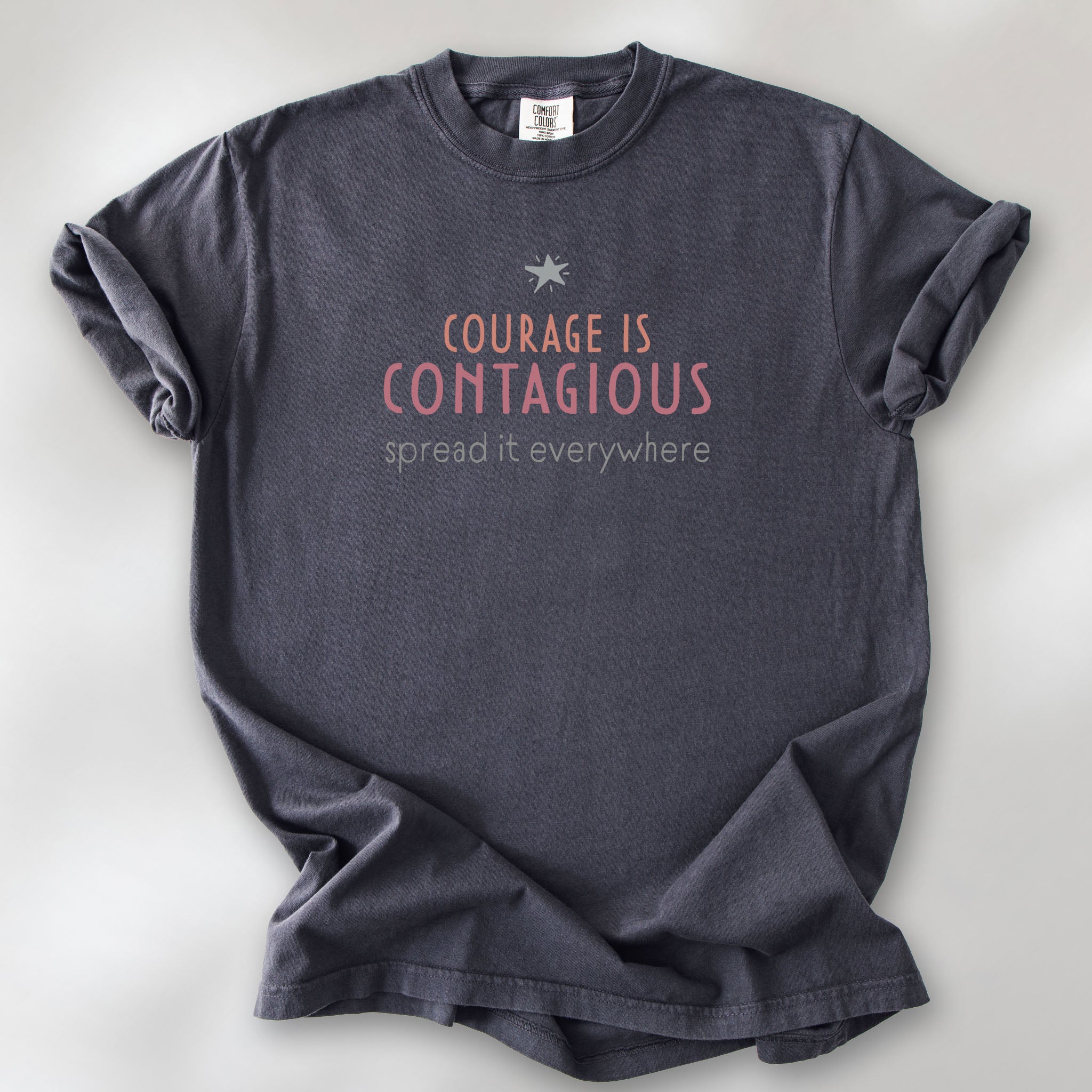 Graphite t-shirt with the words “Courage Is Contagious – Spread It Everywhere” printed in soft pink, coral, and gray.