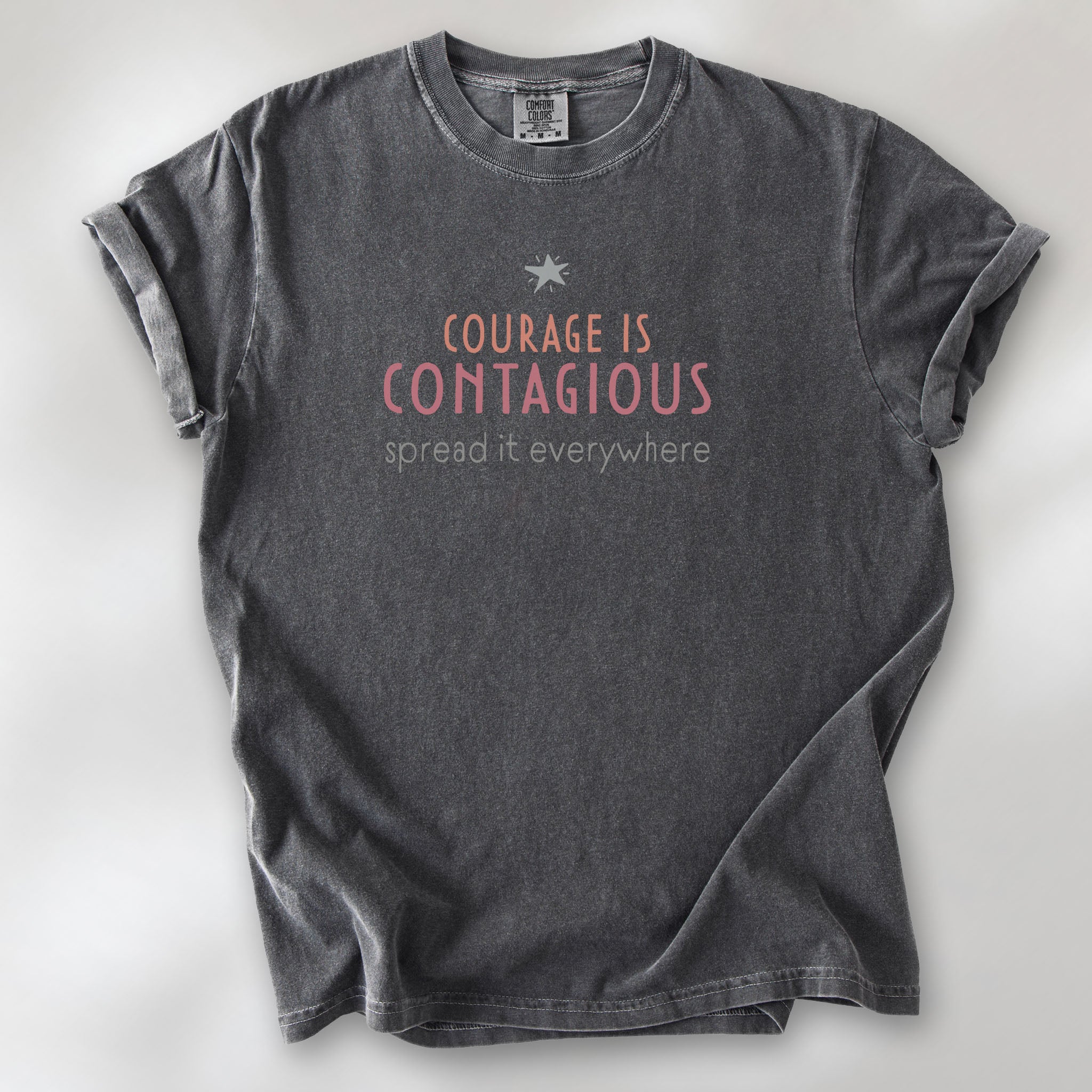 Pepper t-shirt with the words “Courage Is Contagious – Spread It Everywhere” printed in soft pink, coral, and gray.