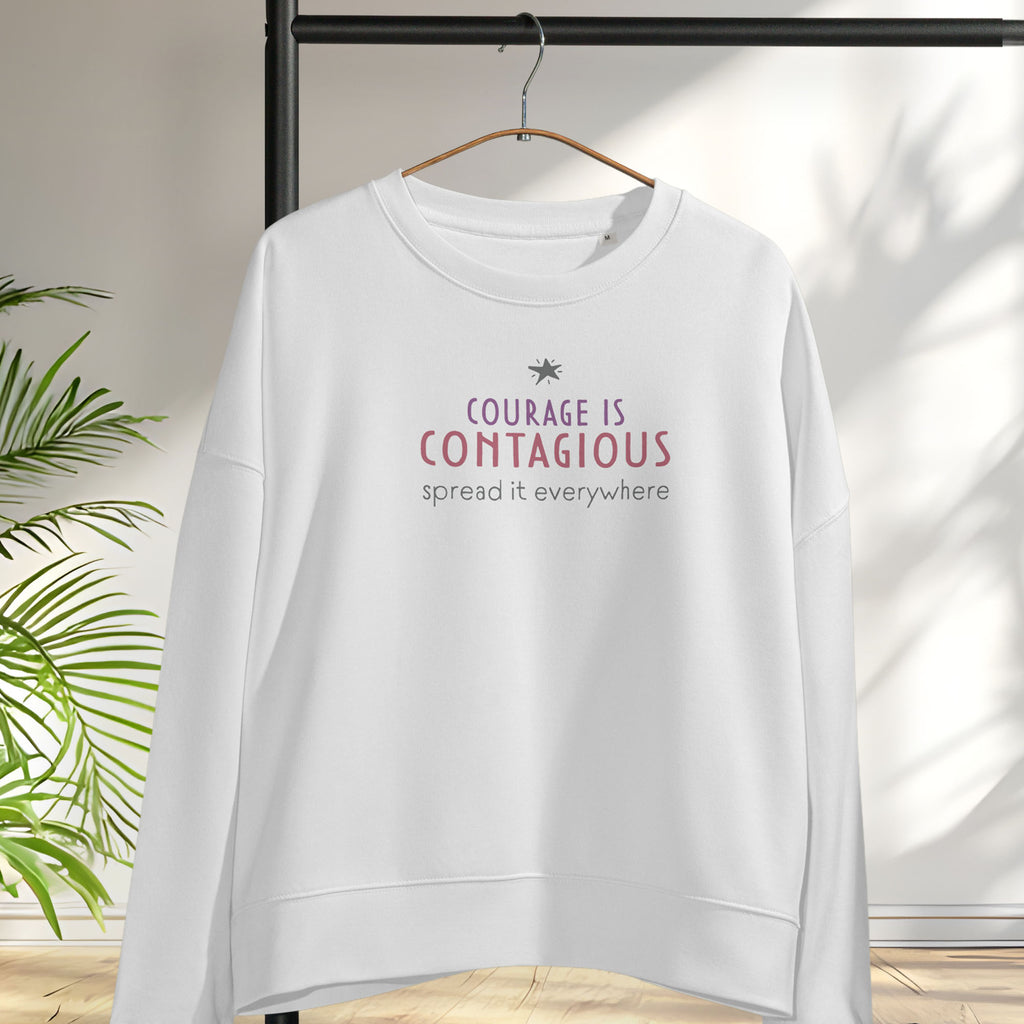 White women's crewneck sweatshirt with minimalist stylized text that reads "courage is contagious – spread it everywhere". Hanging on a hanger.