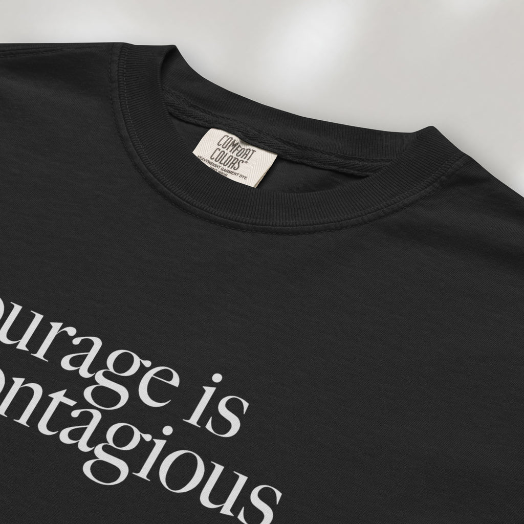 Closeup detail of black t-shirt with minimalist serif text reading “courage is contagious”.