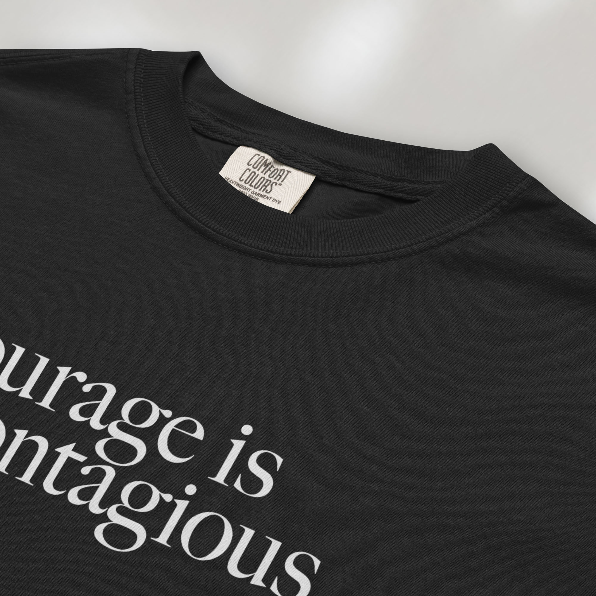 Closeup detail of black t-shirt with minimalist serif text reading “courage is contagious”.