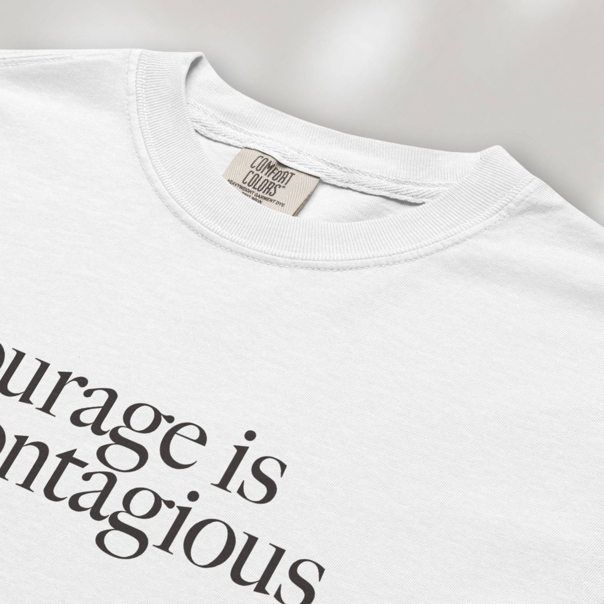 Closeup detail of white t-shirt with minimalist serif text reading “courage is contagious”.