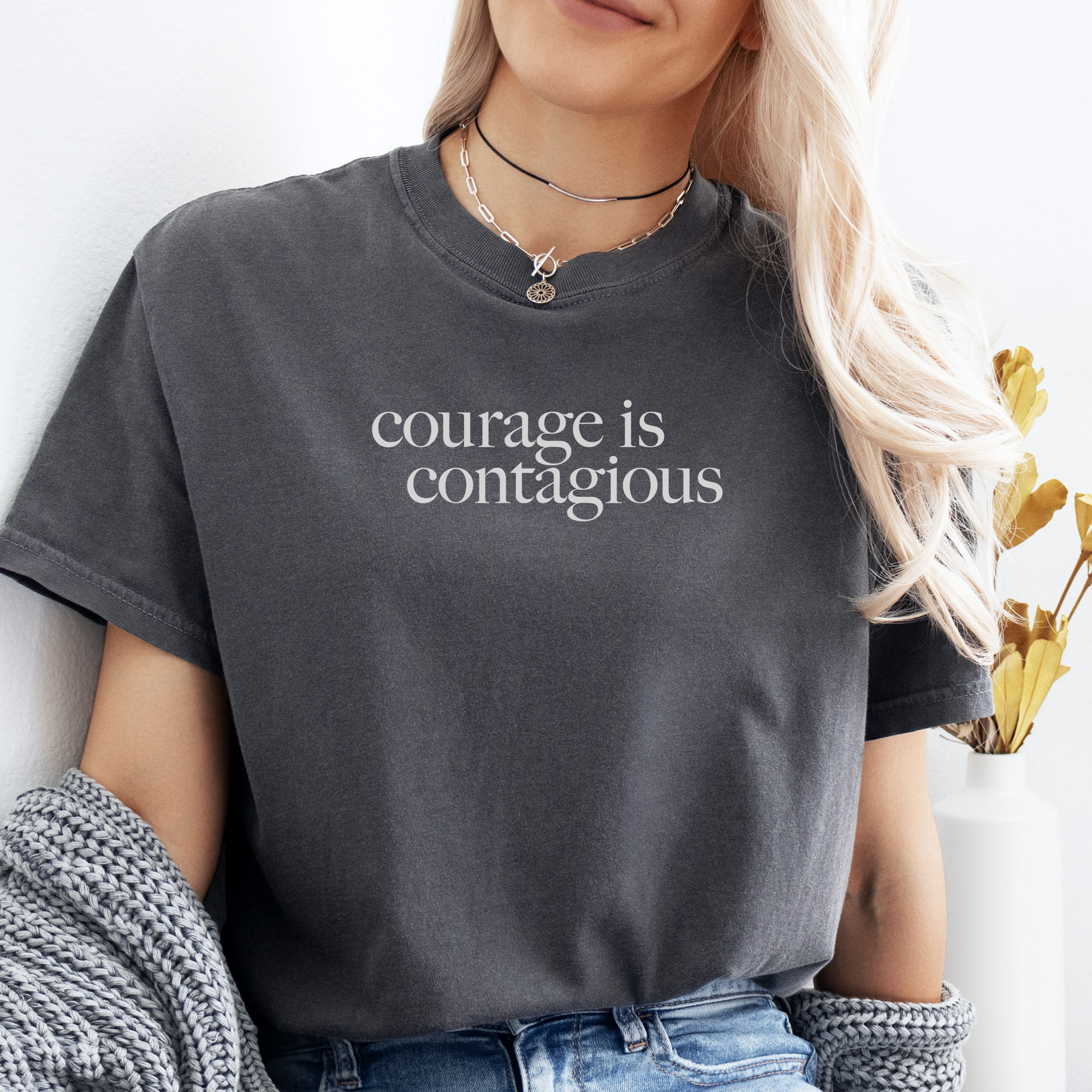 Female model wearing pepper t-shirt with minimalist serif text reading “courage is contagious”.