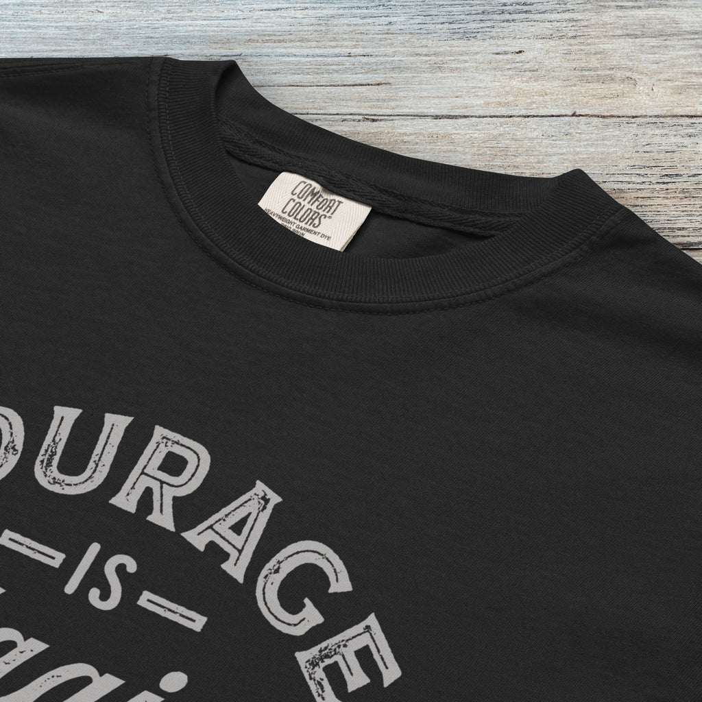 Closeup detail of black vintage style typography shirt reading "Courage Is Contagious Spread It Everywhere" in distressed lettering.