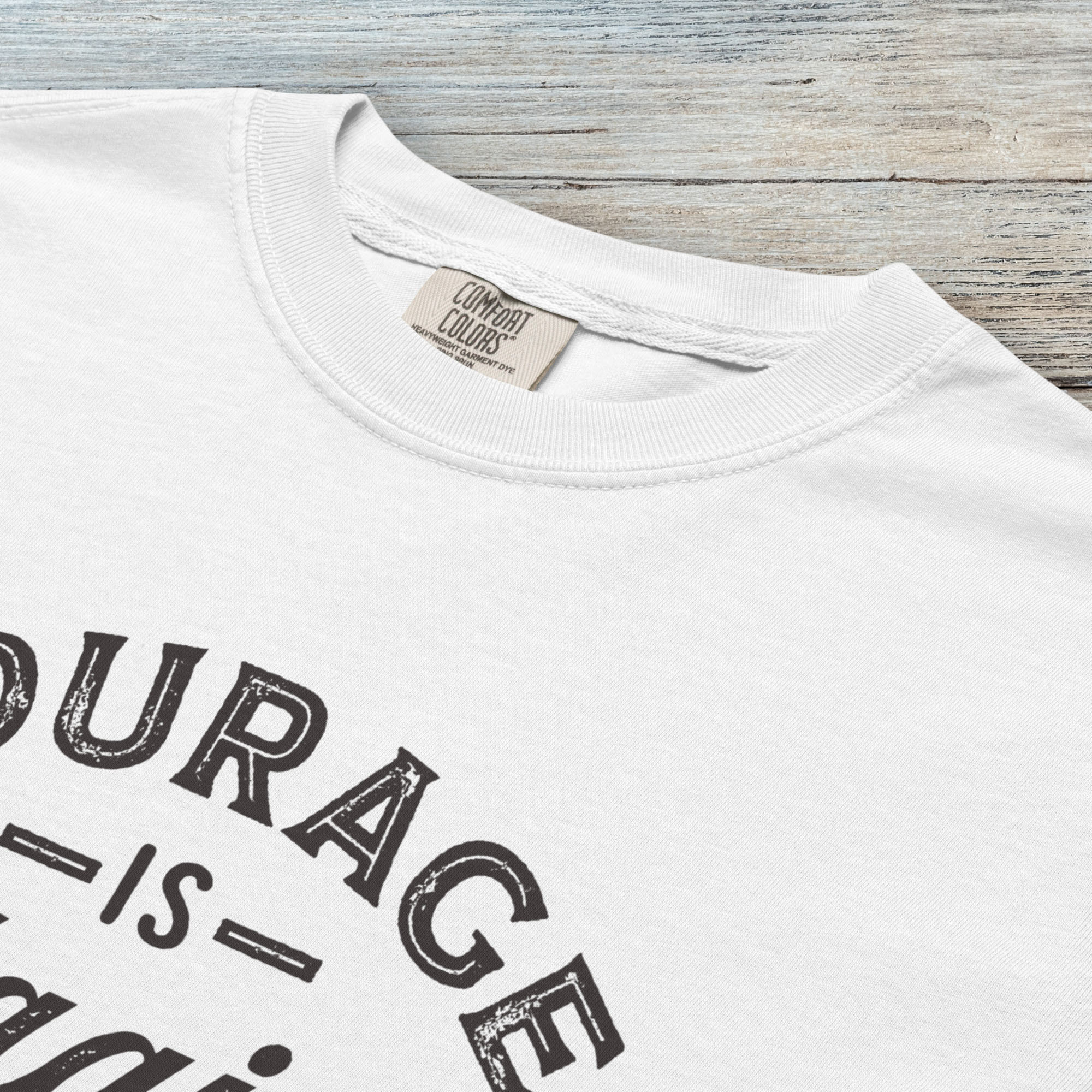 Closeup detail of white vintage style typography shirt reading "Courage Is Contagious Spread It Everywhere" in distressed lettering.