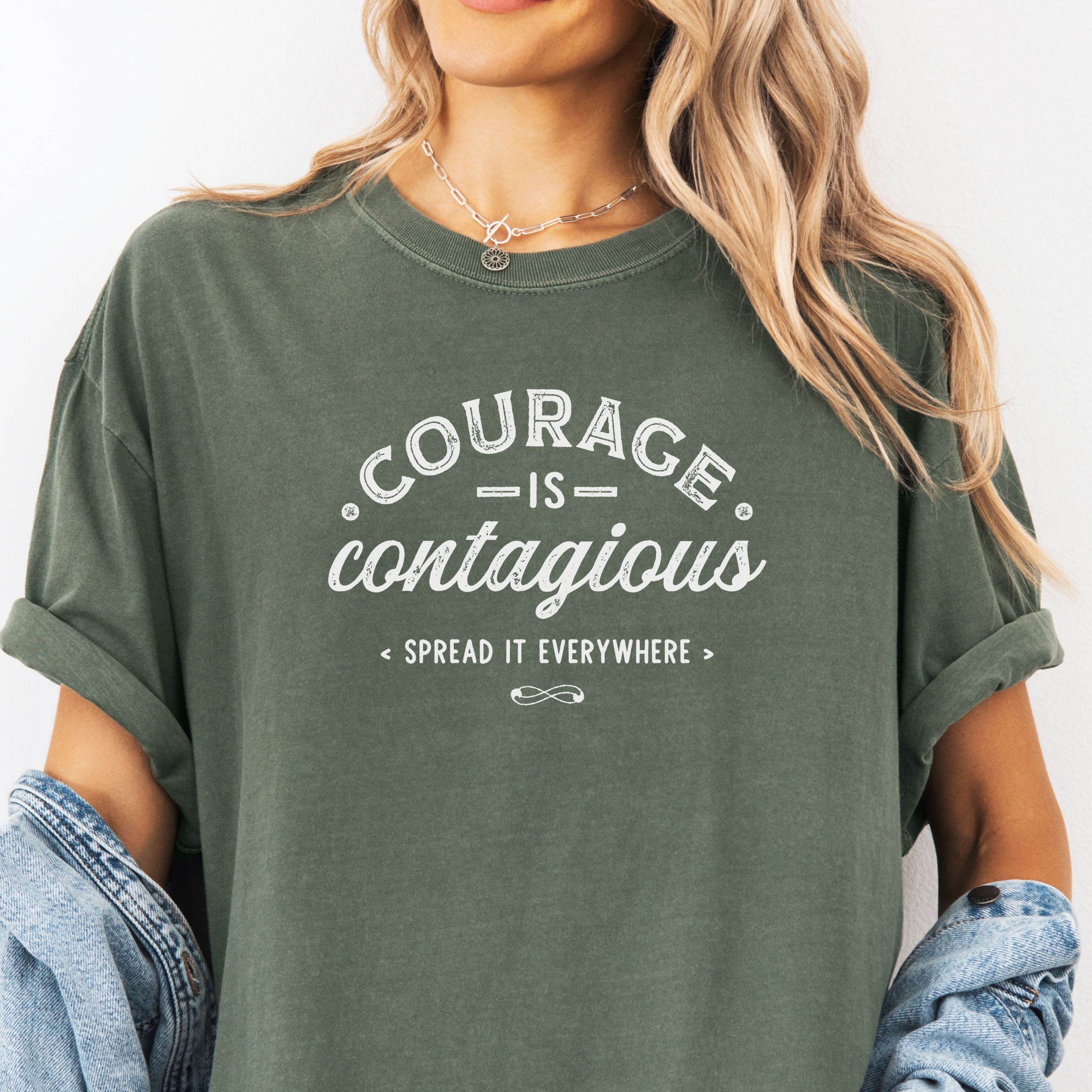 Female model wearing oversized moss vintage style typography shirt reading "Courage Is Contagious Spread It Everywhere" in distressed lettering.