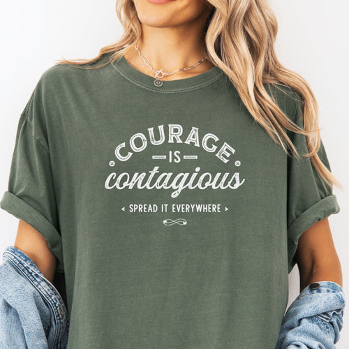 Female model wearing oversized moss vintage style typography shirt reading "Courage Is Contagious Spread It Everywhere" in distressed lettering.