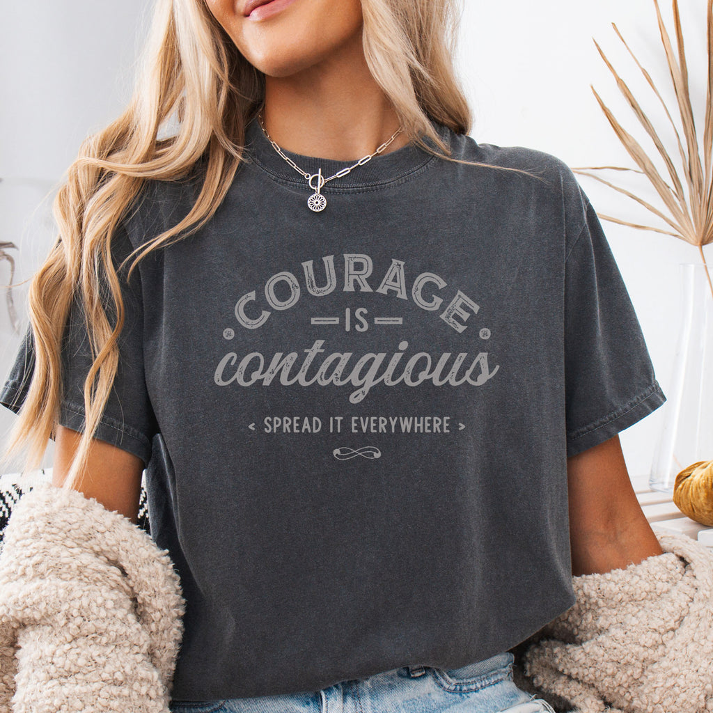Female model wearing pepper vintage style typography shirt reading "Courage Is Contagious Spread It Everywhere" in distressed lettering.