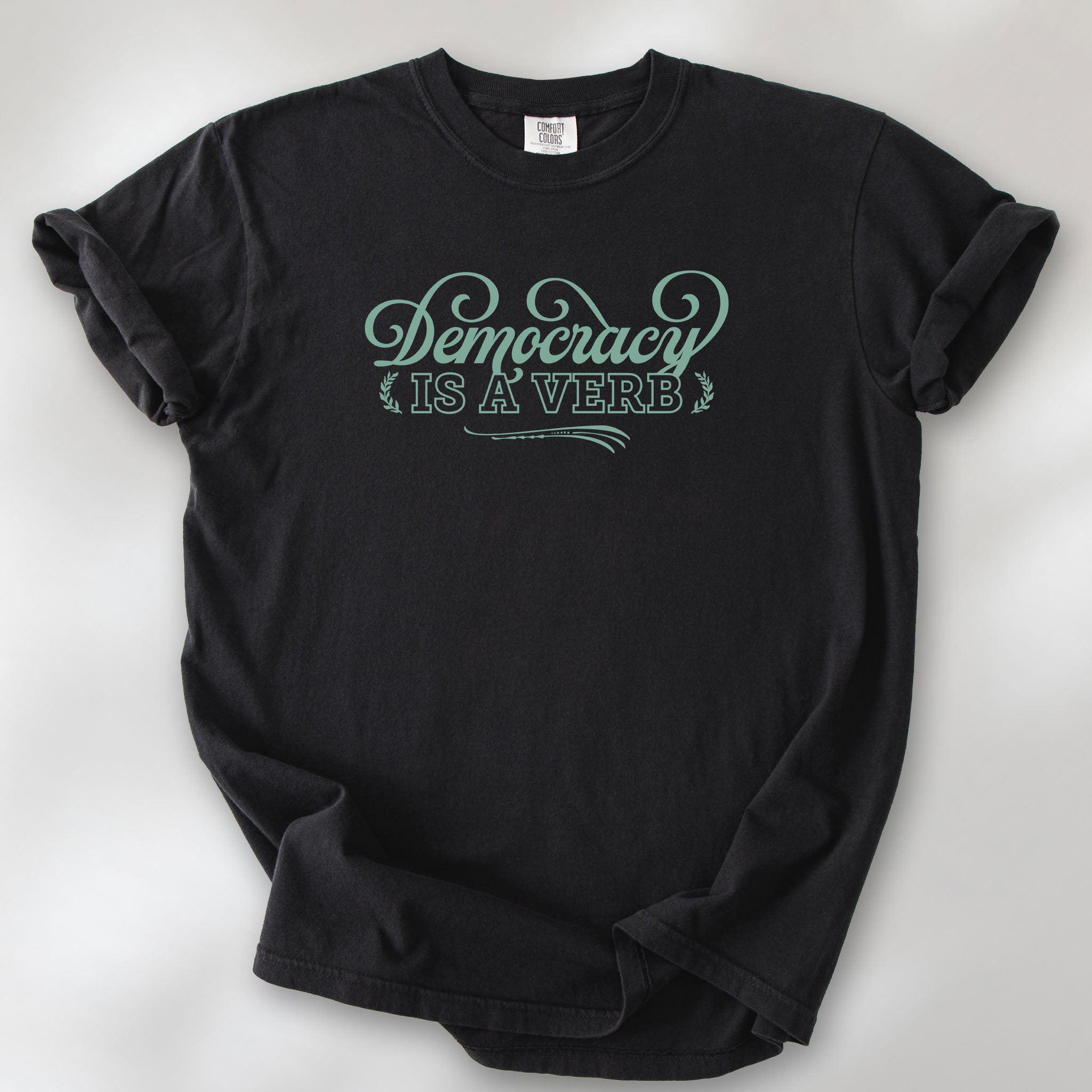 Black t-shirt with the phrase “Democracy Is a Verb” in decorative mint green lettering.
