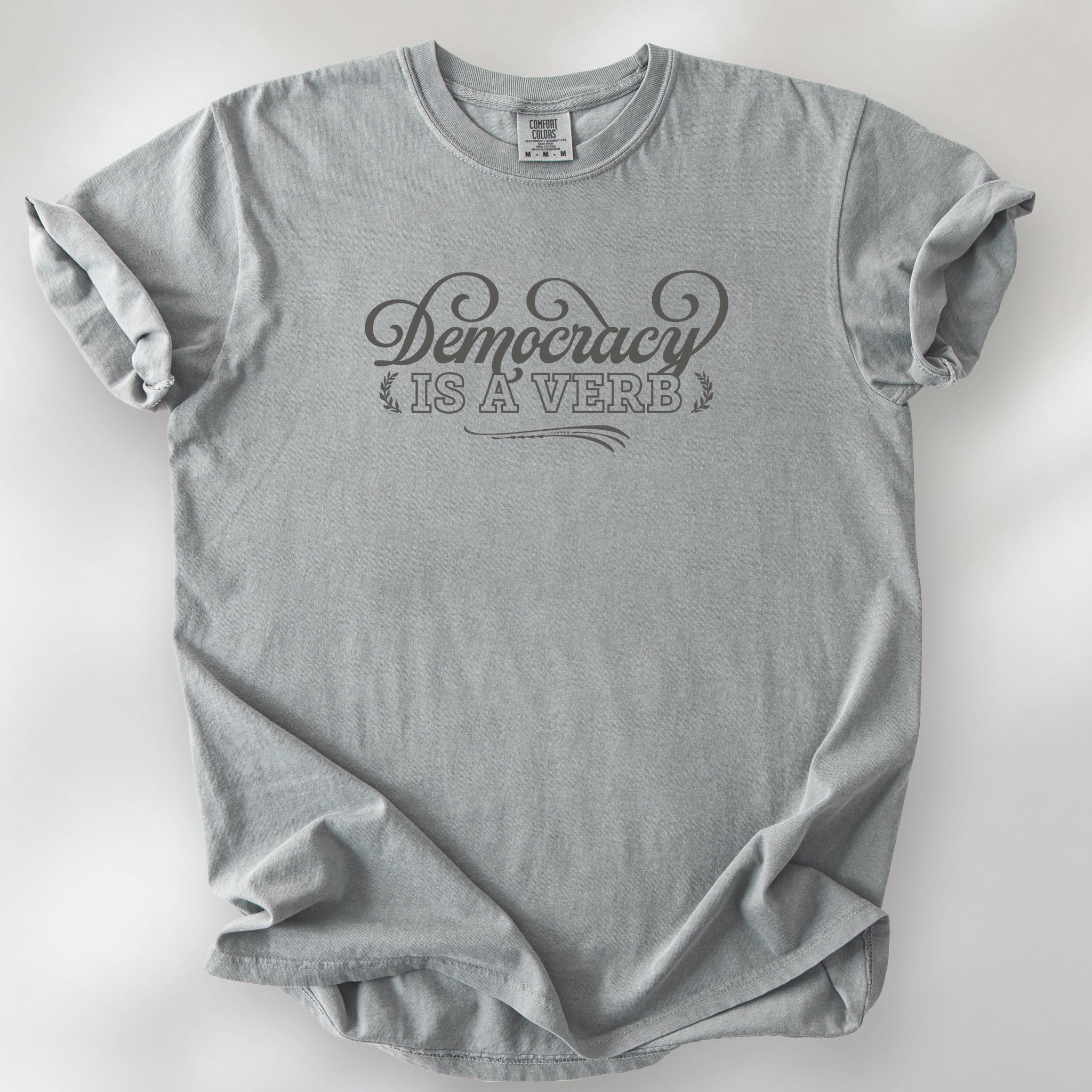 Granite t-shirt with the phrase “Democracy Is a Verb” in decorative mint green lettering.