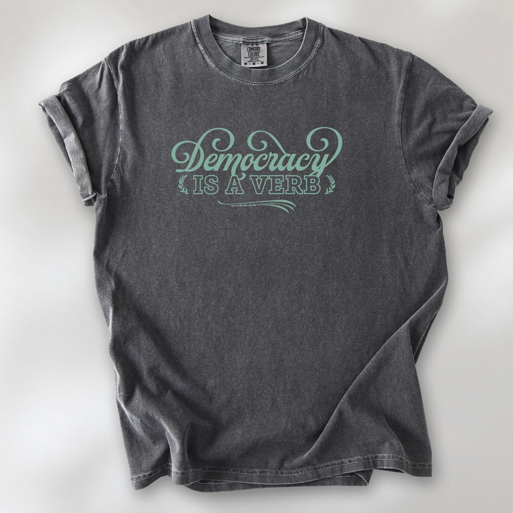 Pepper t-shirt with the phrase “Democracy Is a Verb” in decorative mint green lettering.