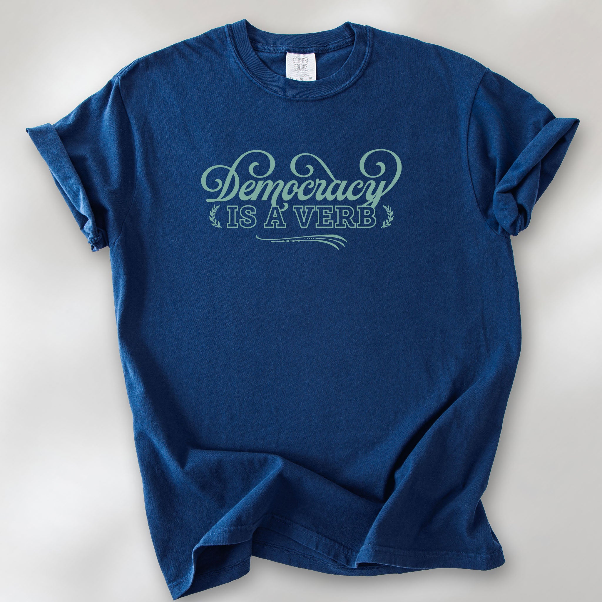 True navy t-shirt with the phrase “Democracy Is a Verb” in decorative mint green lettering.