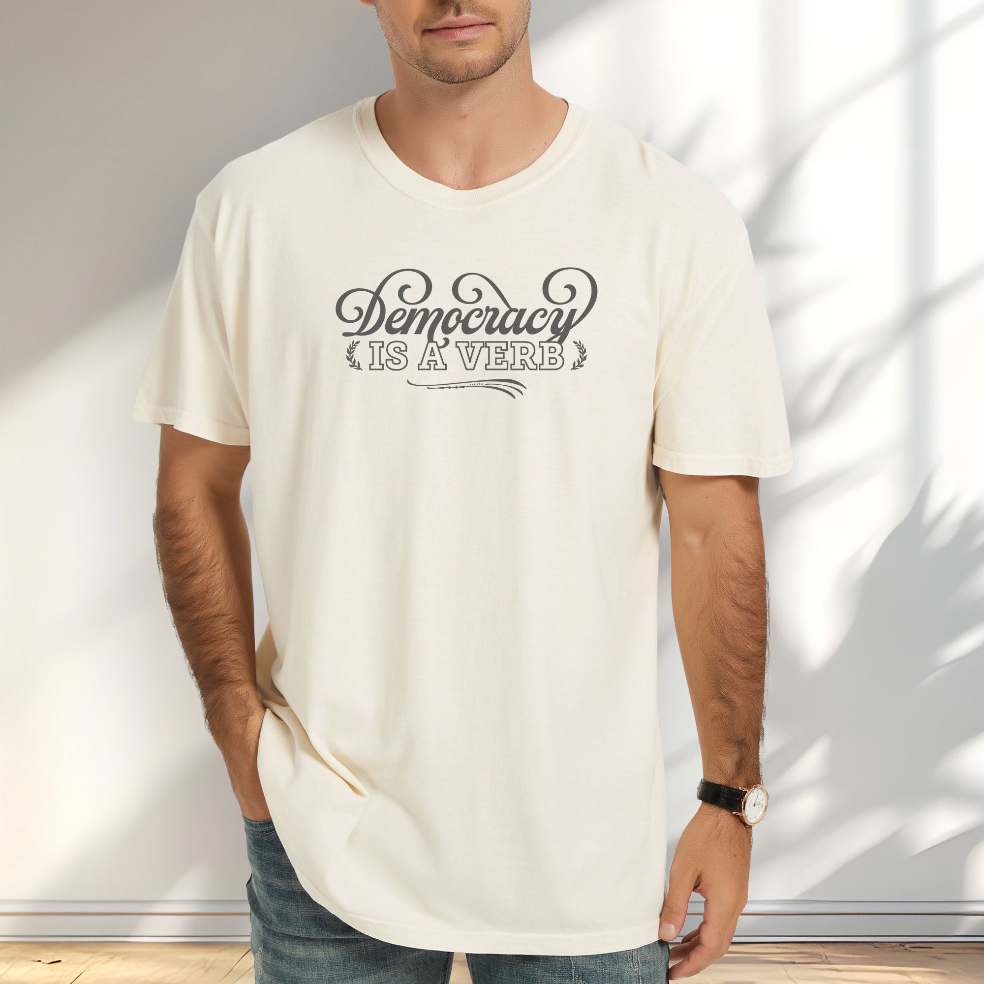 Male model wearing ivory t-shirt with the phrase “Democracy Is a Verb” in decorative mint green lettering.