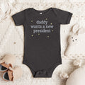 Dark grey heather baby short sleeve one piece with white text reading “daddy wants a new president."