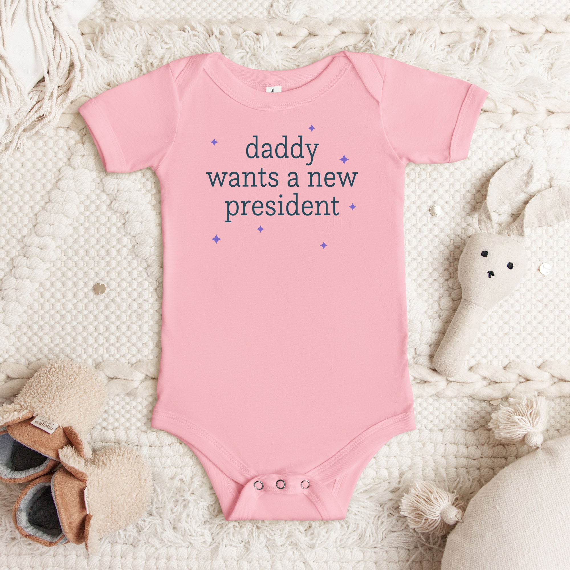 Pink baby short sleeve one piece with dark text reading “mommy wants a new president."