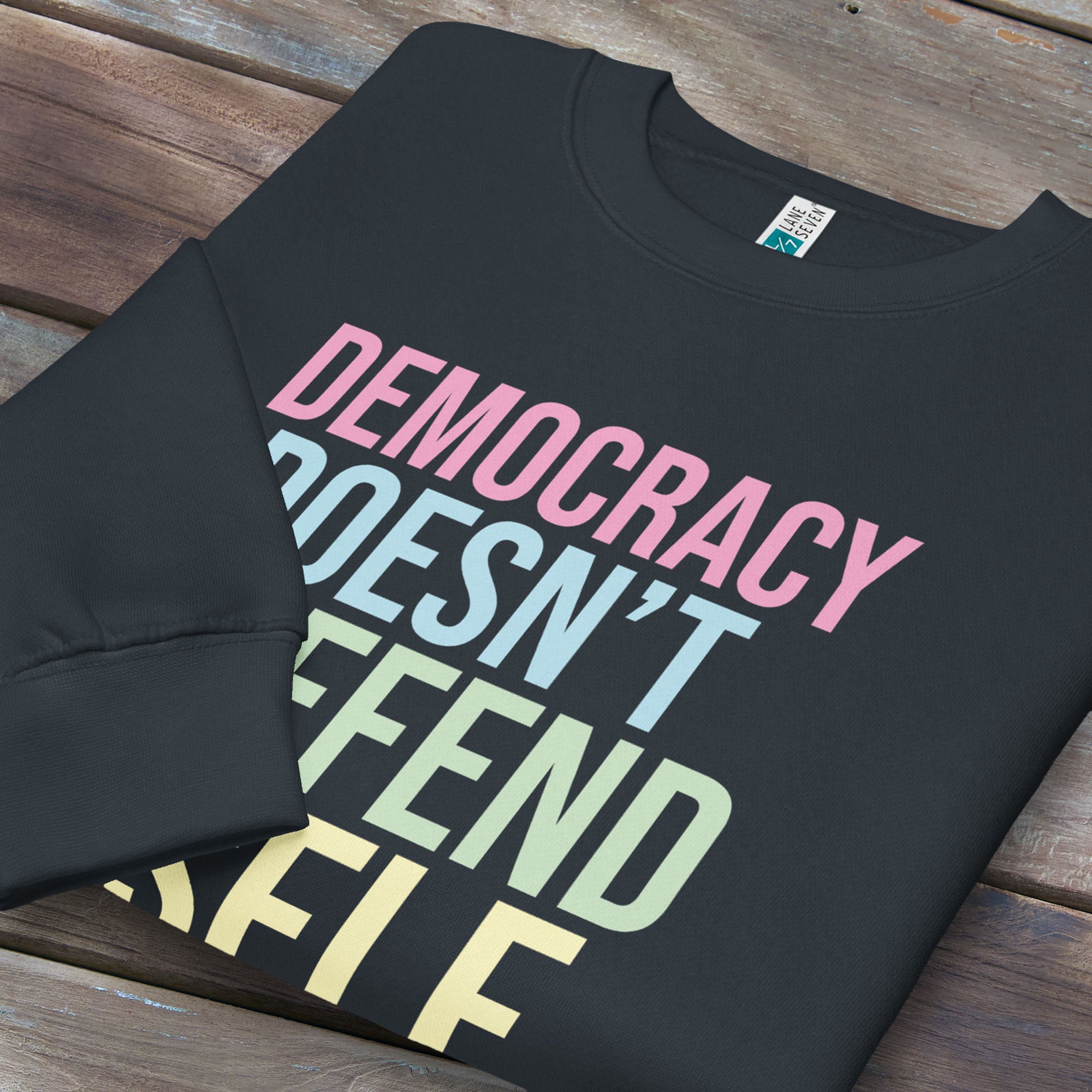 Folded navy sweatshirt that says “Democracy Doesn’t Defend Itself” in pink, blue, green, and yellow.