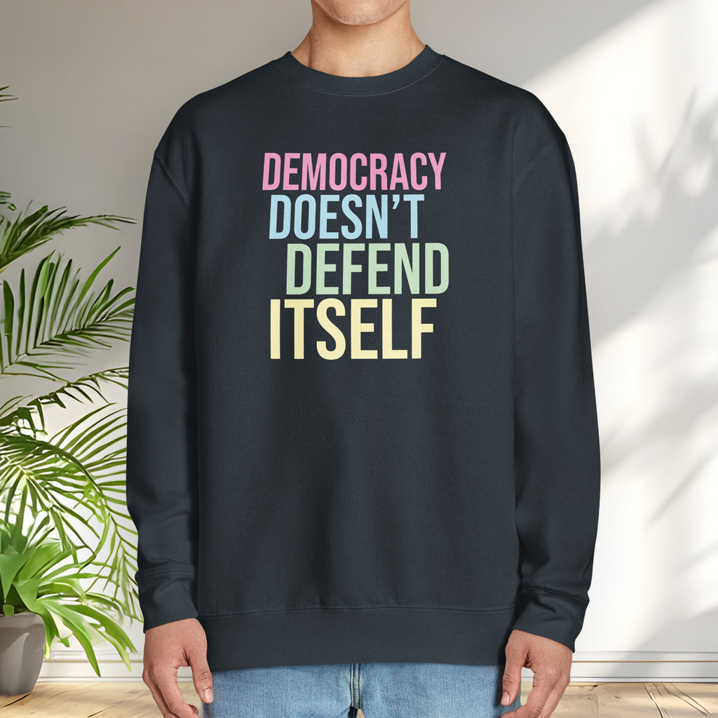Male model wearing navy sweatshirt that says “Democracy Doesn’t Defend Itself” in pink, blue, green, and yellow.