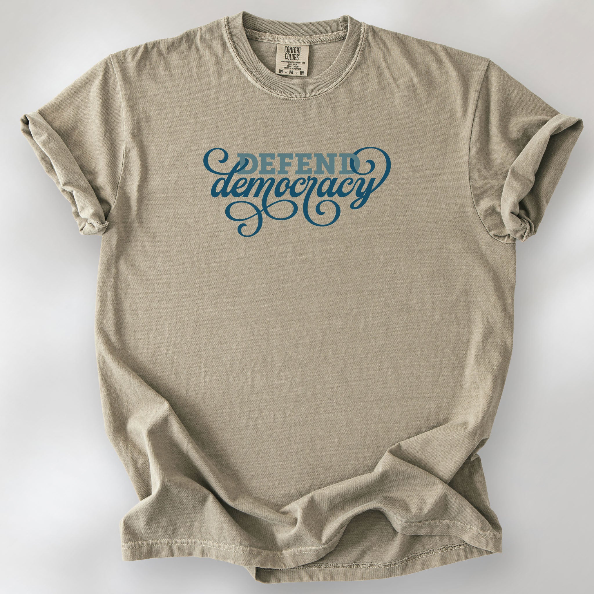Khaki t-shirt with blue slab and script text reading “Defend Democracy.”