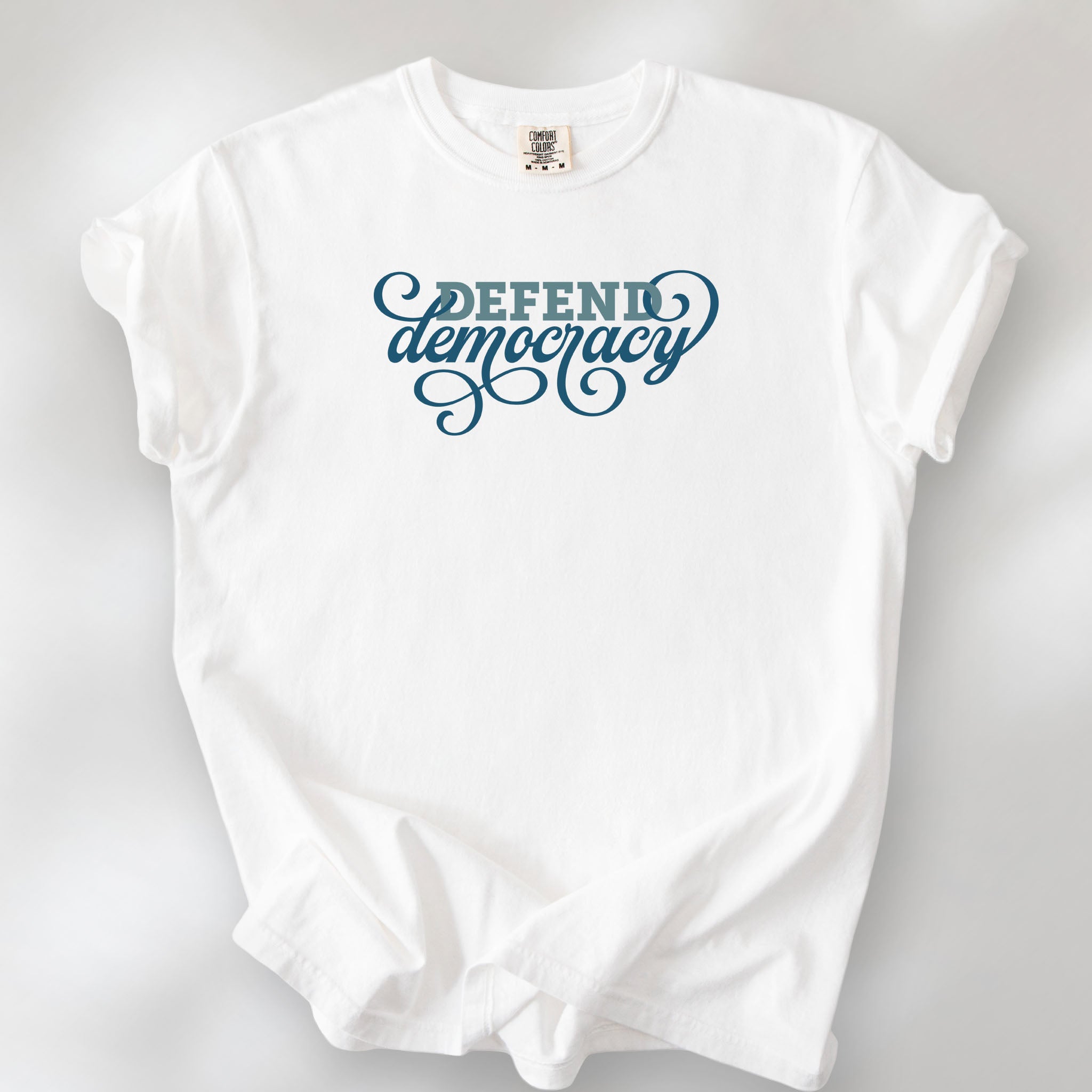 White t-shirt with blue slab and script text reading “Defend Democracy.”