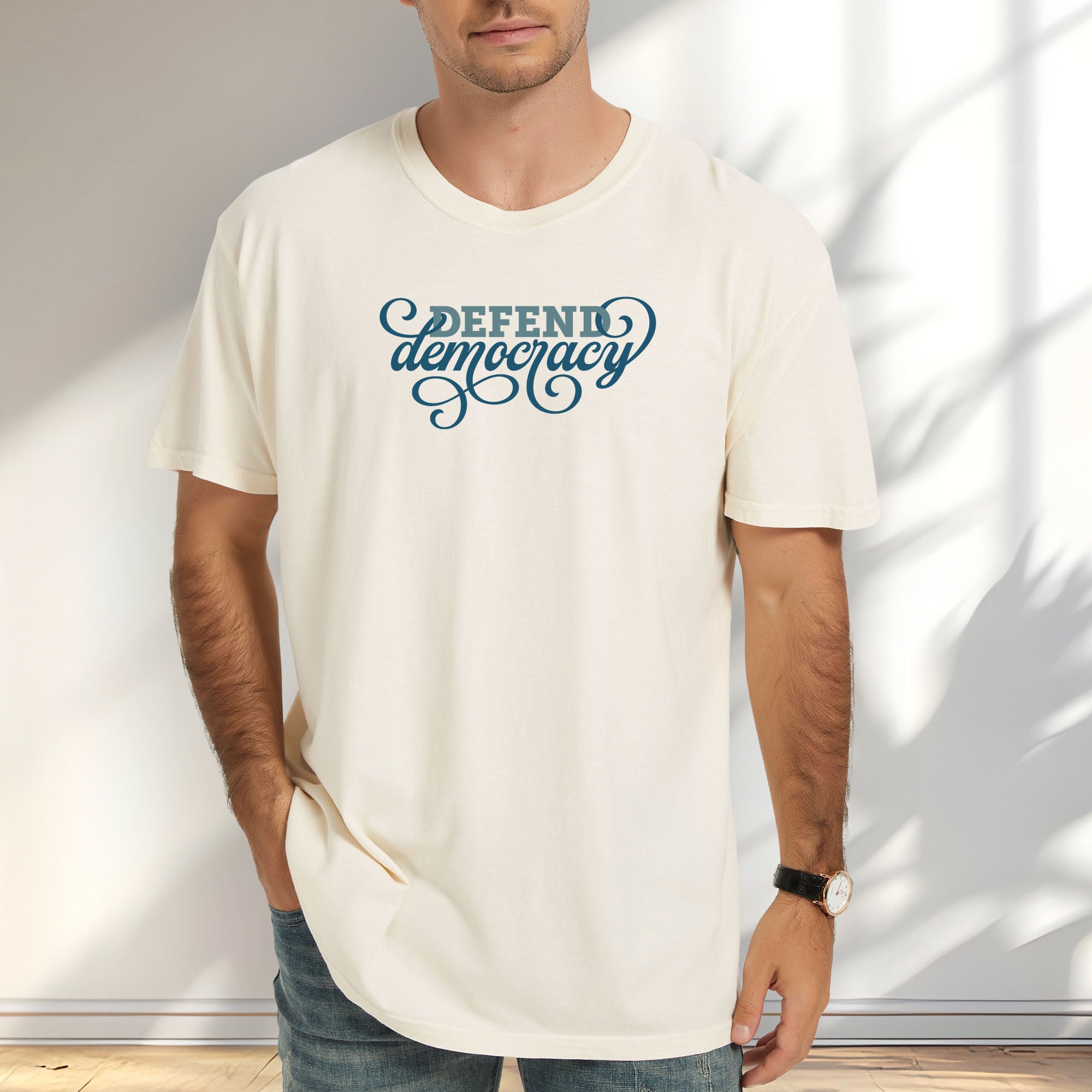 Male model wearing ivory t-shirt with blue slab and script text reading “Defend Democracy.”