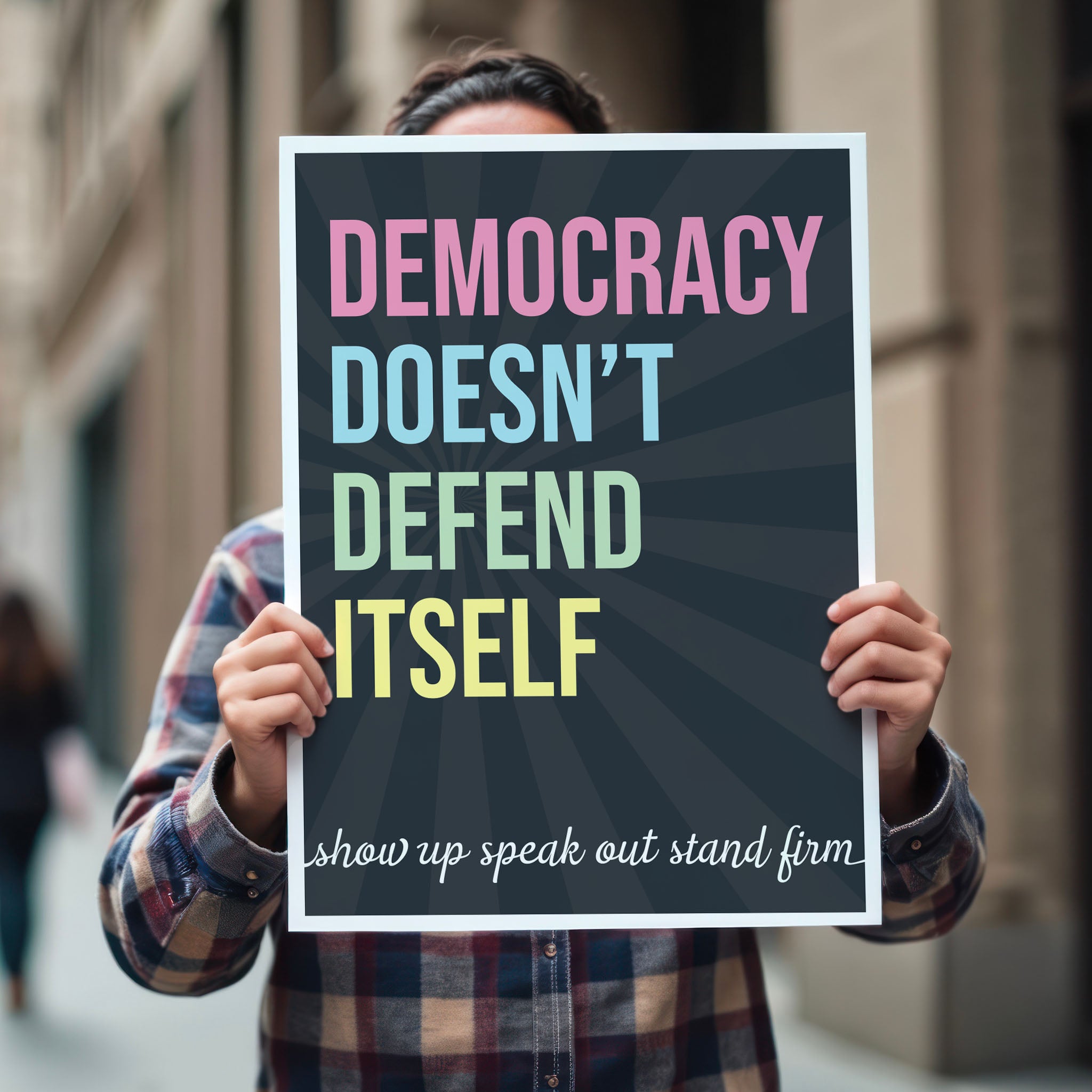 Person holding protest sign with dark background with subtle burst, bold colorful text that reads "democracy doesn't defend itself", then white script text near the bottom that reads "show up, speak out, stand firm."