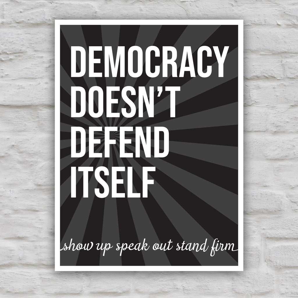 Black and white version of protest sign with dark background with subtle burst, bold text that reads "democracy doesn't defend itself", then white script text near the bottom that reads "show up, speak out, stand firm."