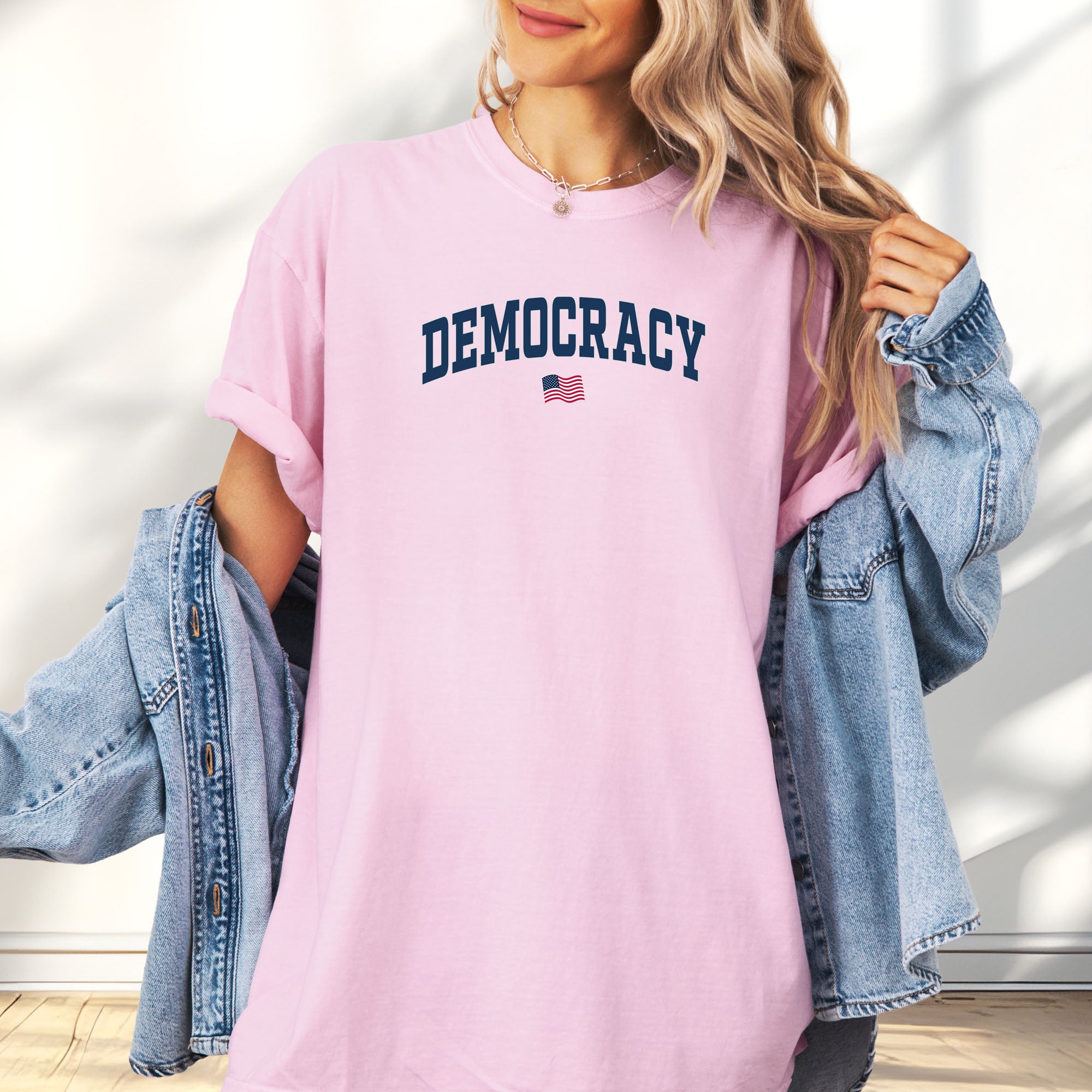 Female model wearing blossom t-shirt with the word “Democracy” in bold navy letters and a small American flag underneath, symbolizing U.S. pride in democracy over authoritarianism, tyranny, dictators.