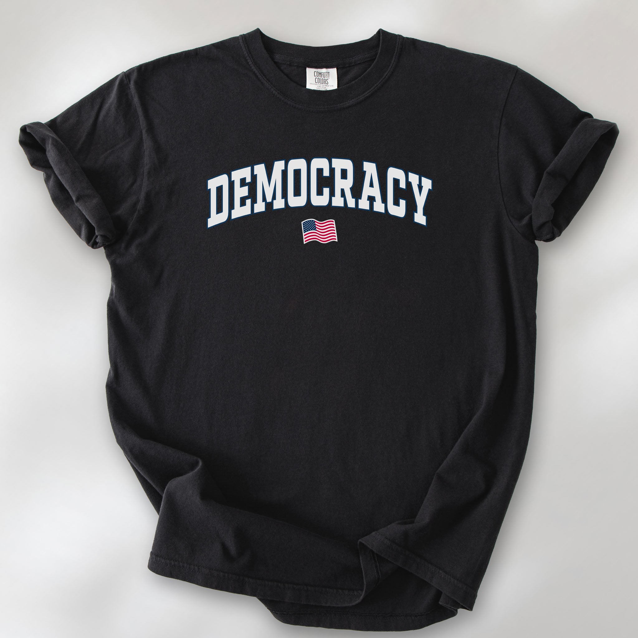 Black t-shirt with varsity-style graphic that says "democracy" with a USA flag beneath it.