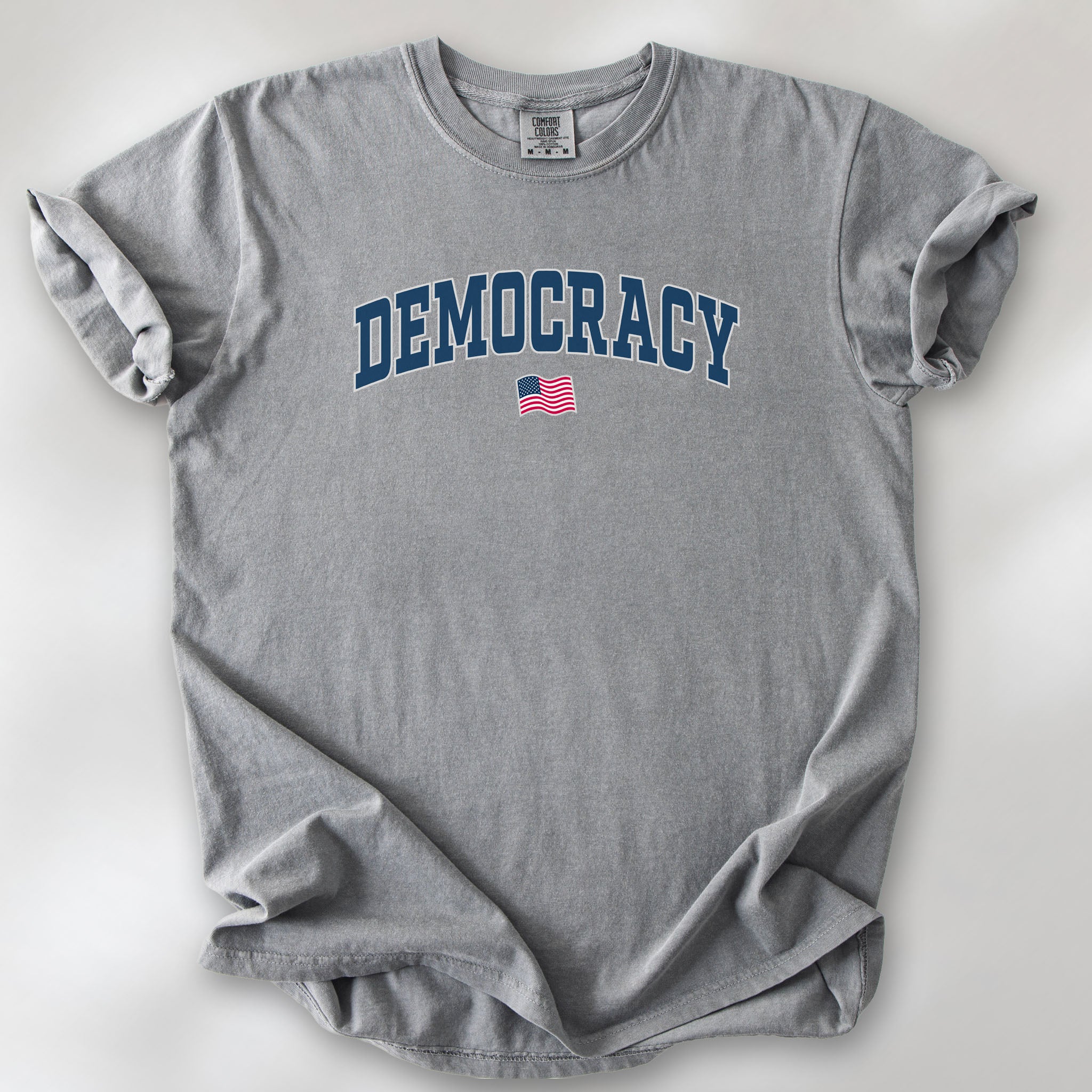 Grey t-shirt with varsity-style graphic that says "democracy" with a USA flag beneath it.