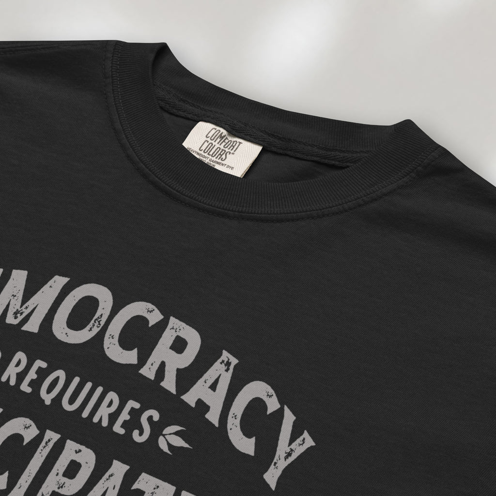 Closeup detail of black t-shirt with vintage style typography reading “Democracy Requires Participation — Show Up Speak Out”.