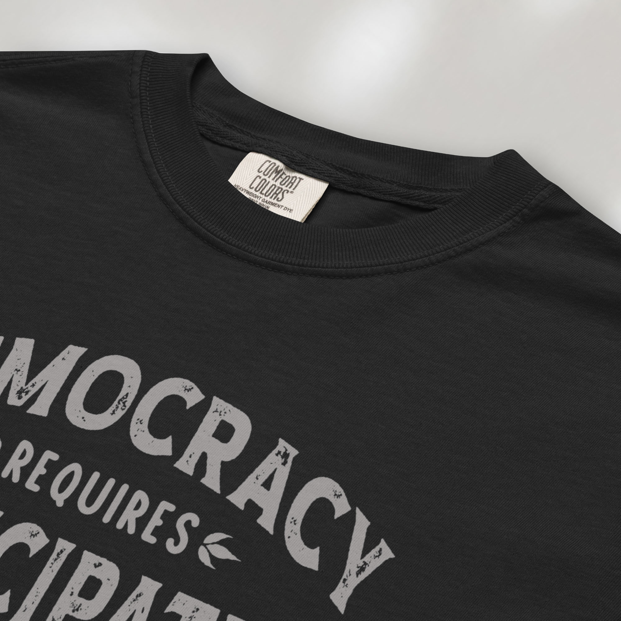 Closeup detail of black t-shirt with vintage style typography reading “Democracy Requires Participation — Show Up Speak Out”.