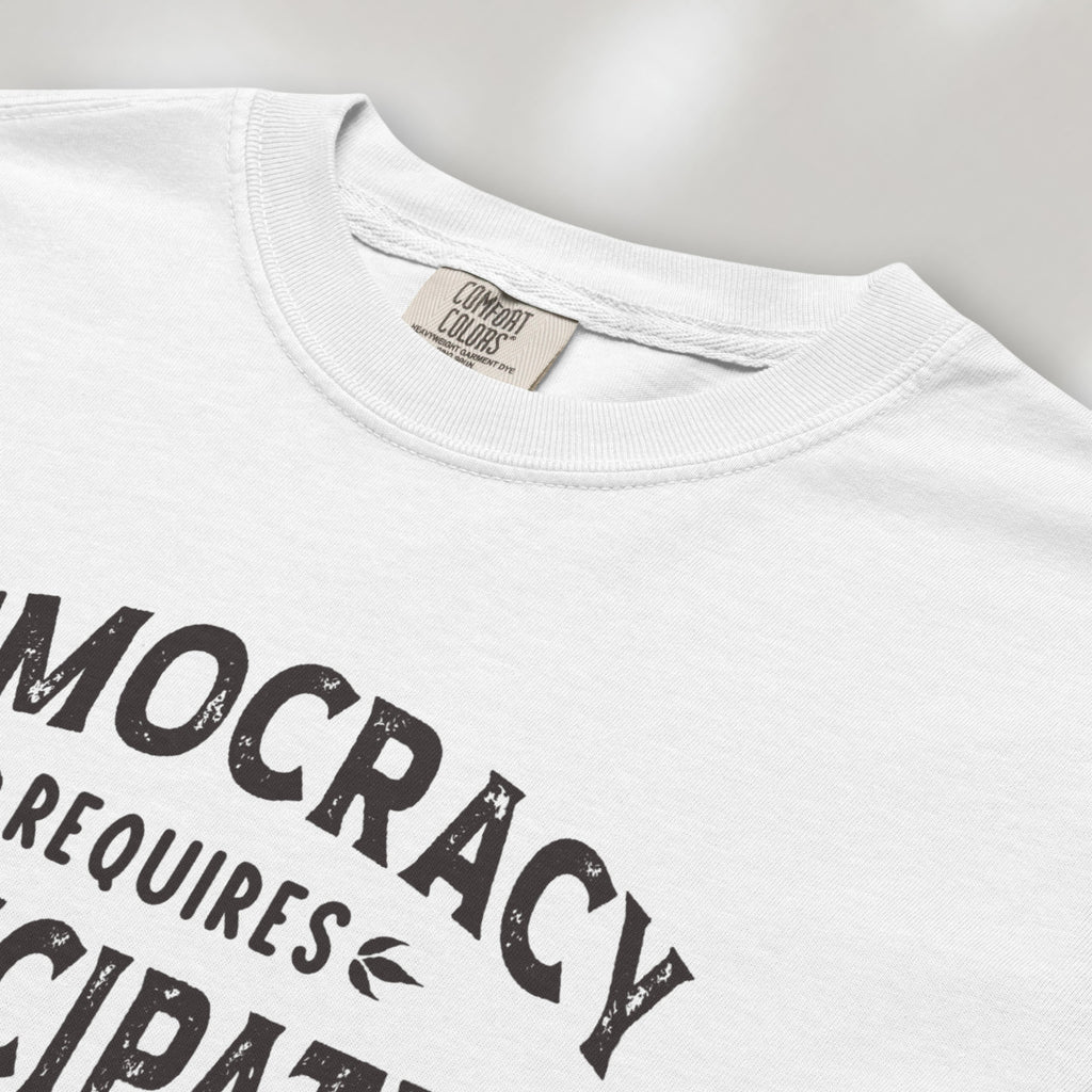 Closeup detail of white t-shirt with vintage style typography reading “Democracy Requires Participation — Show Up Speak Out”.