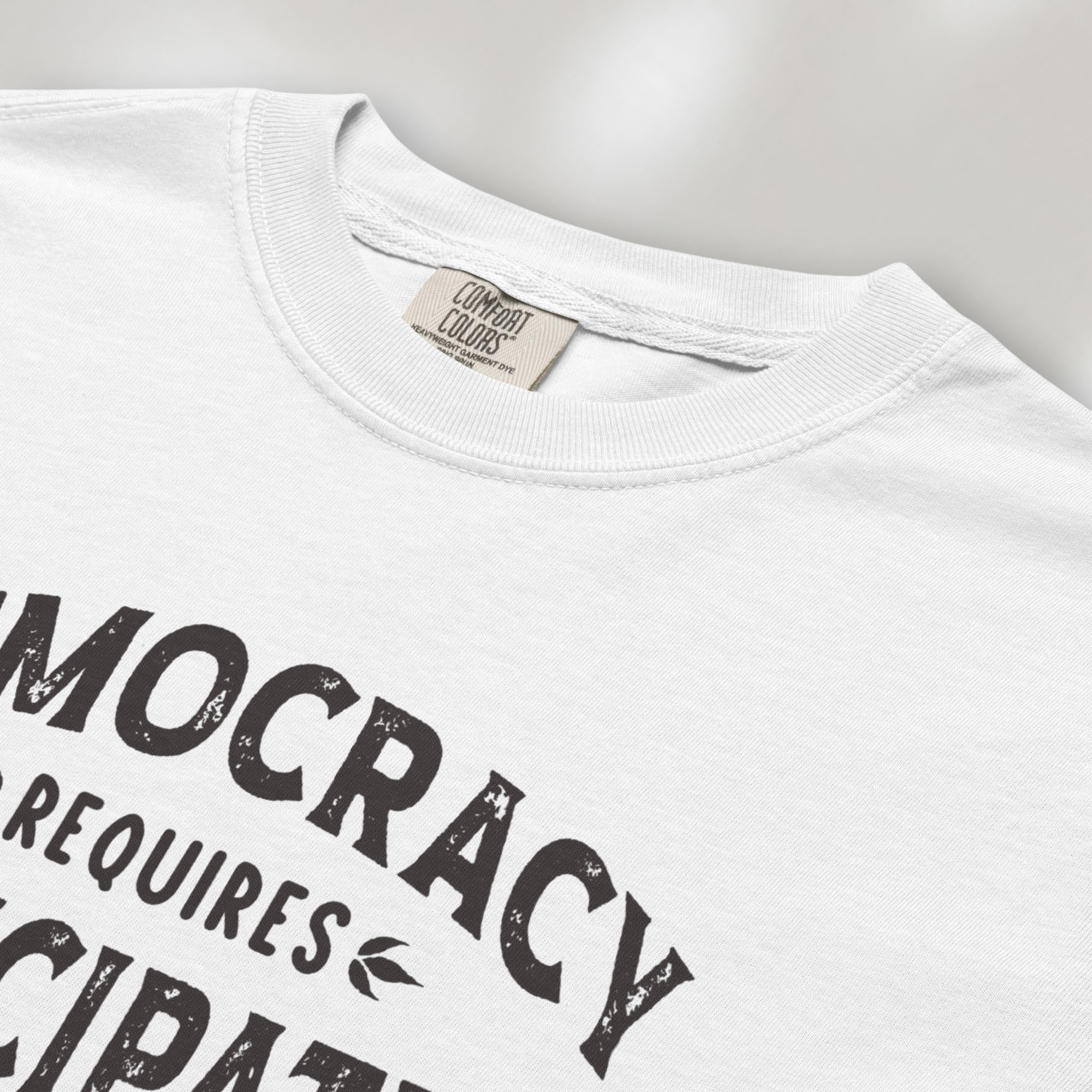 Closeup detail of white t-shirt with vintage style typography reading “Democracy Requires Participation — Show Up Speak Out”.