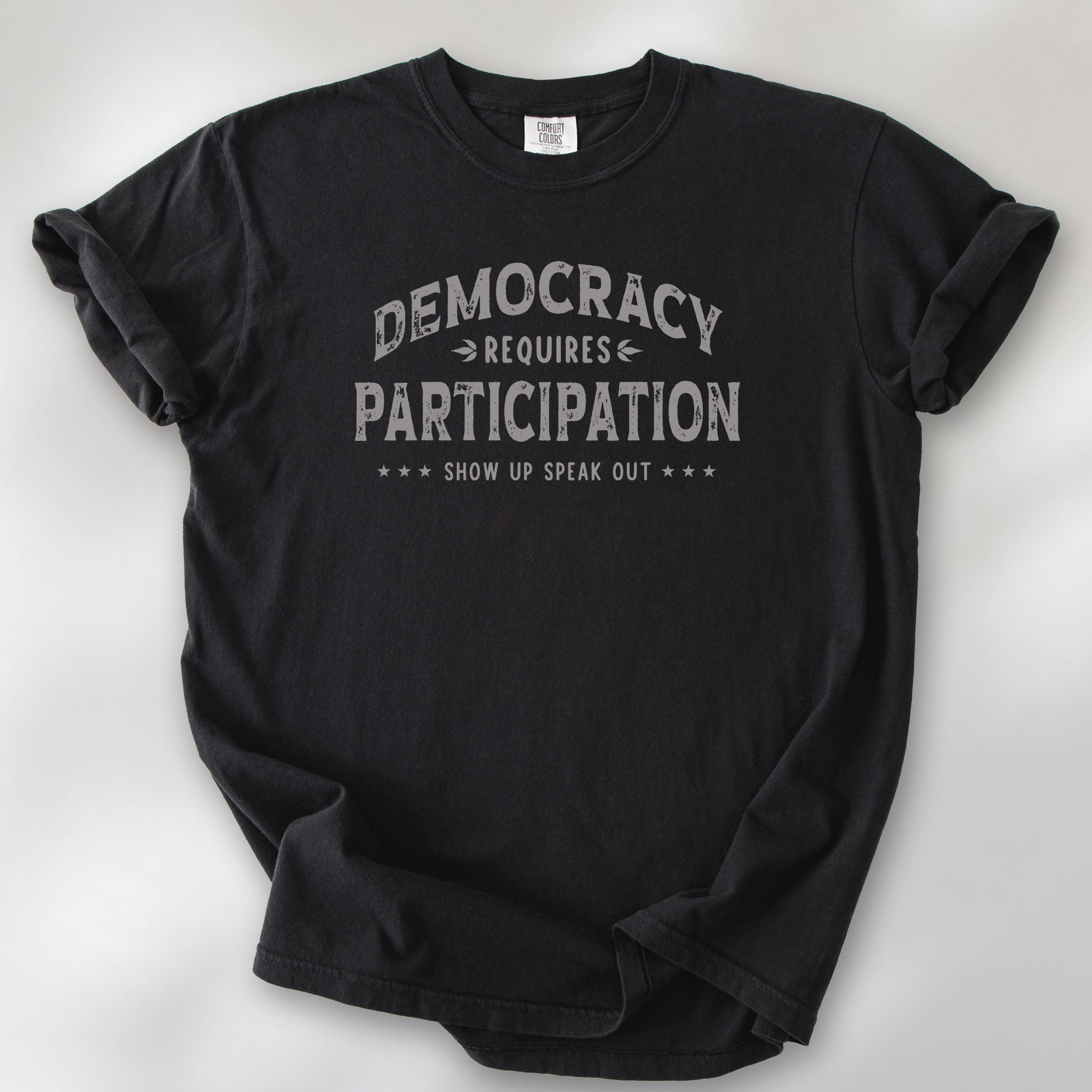 Black t-shirt with vintage style typography reading “Democracy Requires Participation — Show Up Speak Out”.