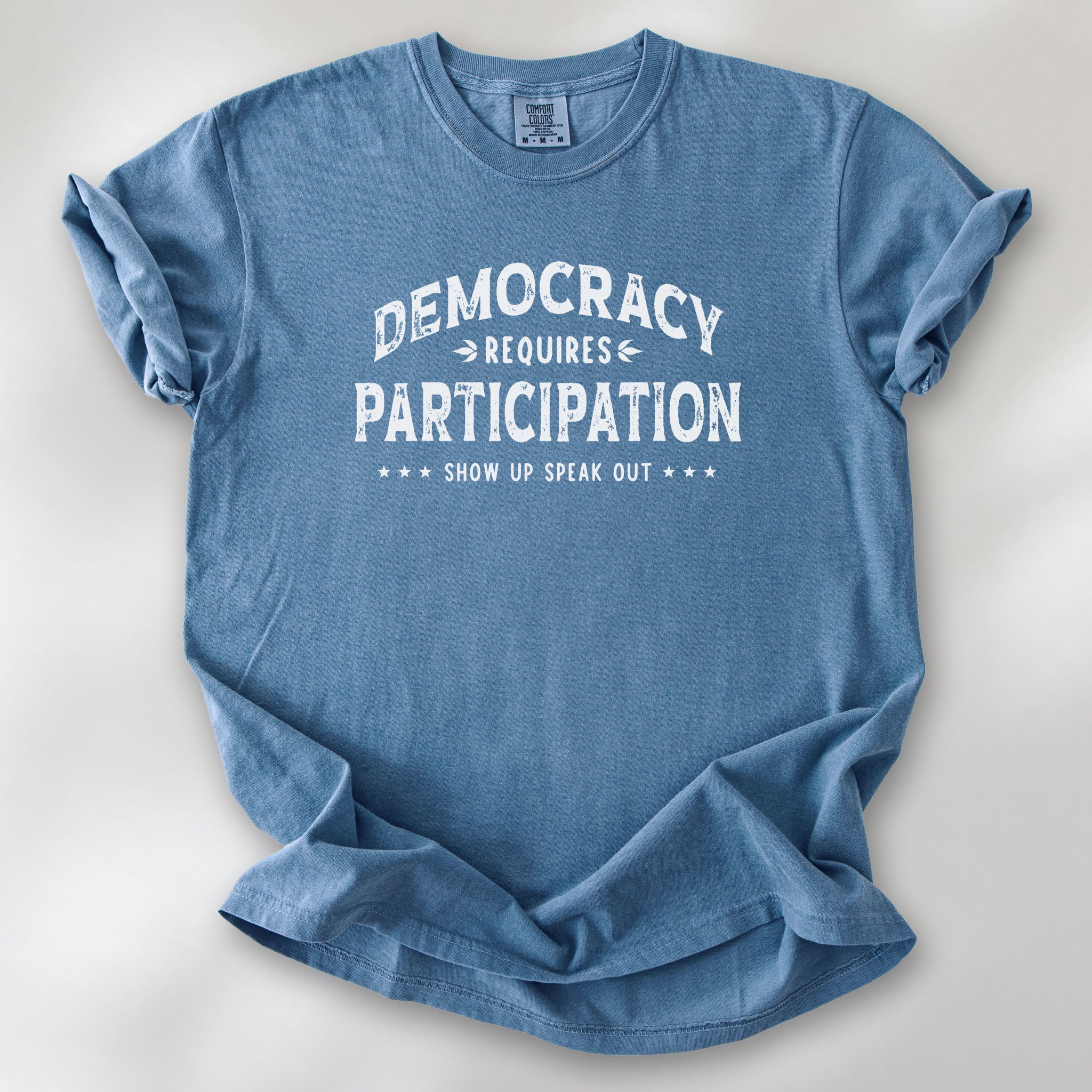 Blue jean t-shirt with vintage style typography reading “Democracy Requires Participation — Show Up Speak Out”.