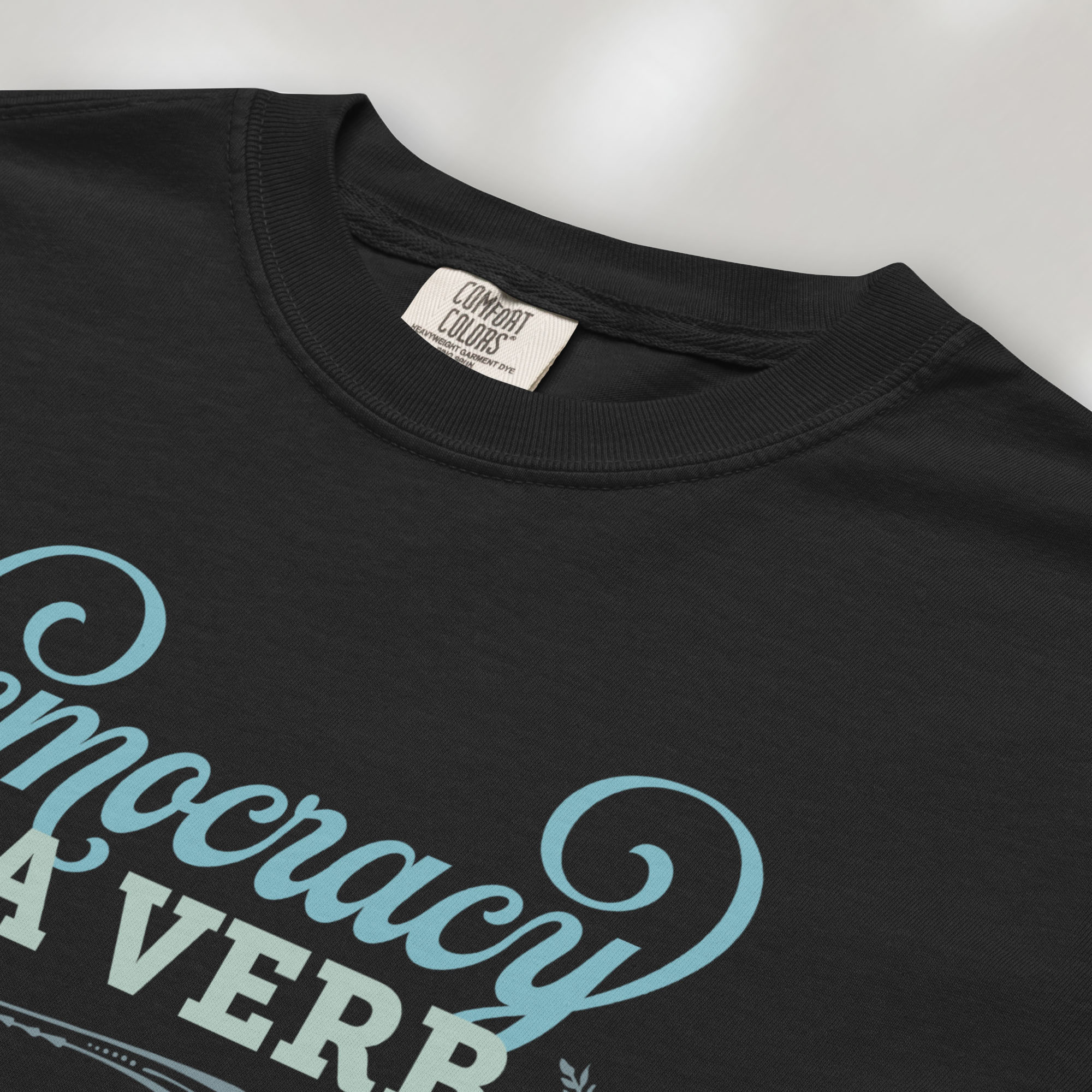 Closeup detail of black t-shirt with the phrase “Democracy Is a Verb” in decorative lettering.