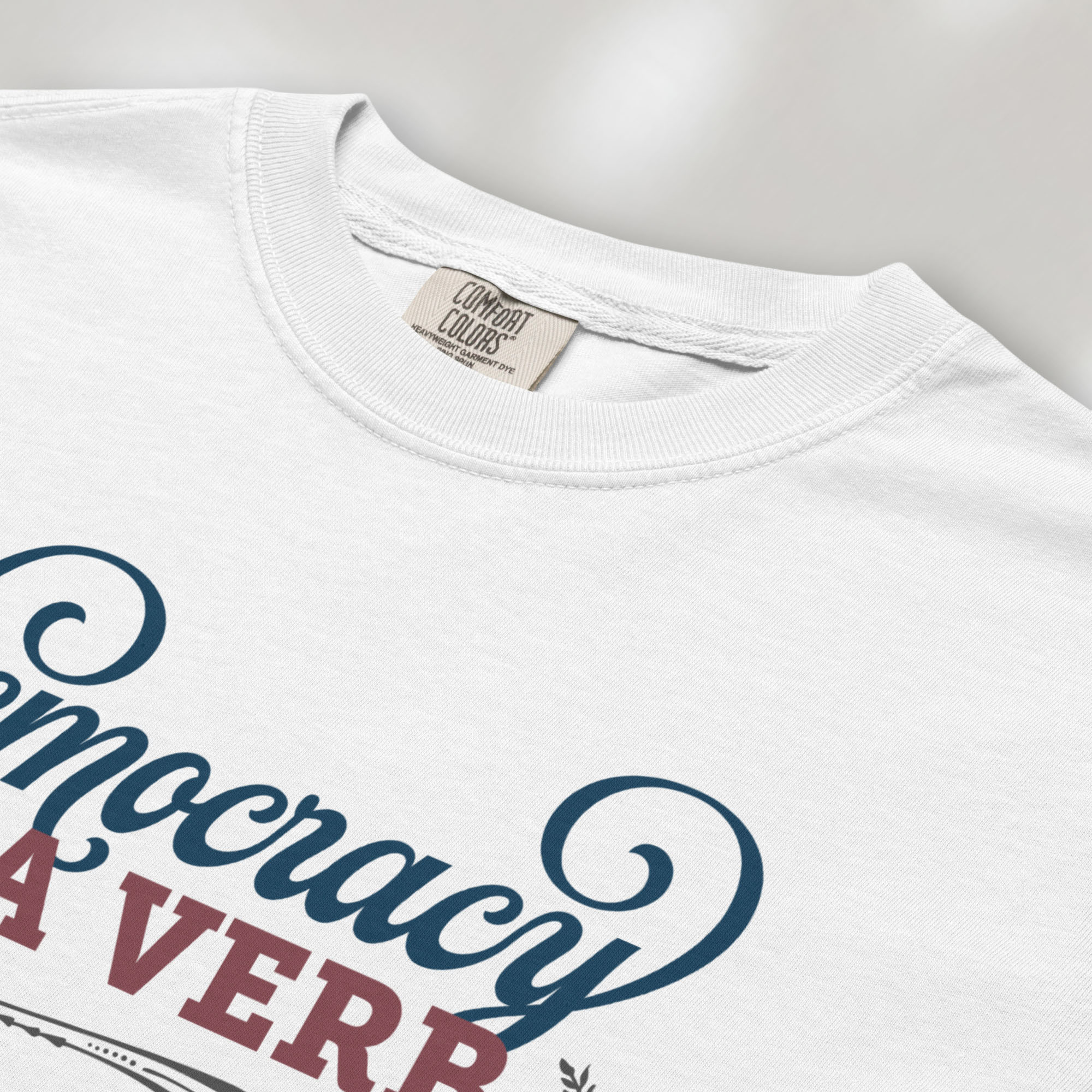 Closeup detail of white t-shirt with the phrase “Democracy Is a Verb” in decorative lettering.