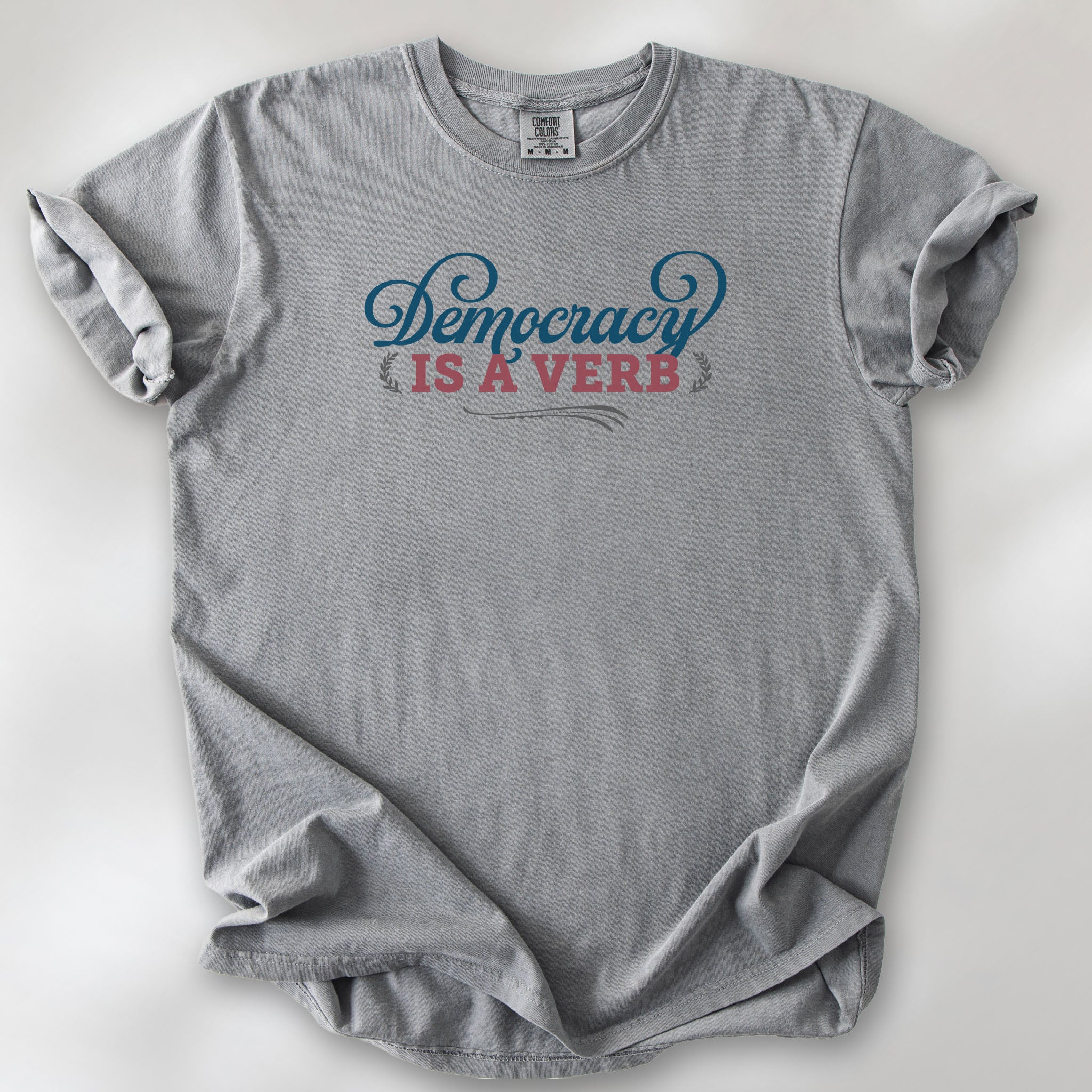 Grey t-shirt with the phrase “Democracy Is a Verb” in decorative lettering.
