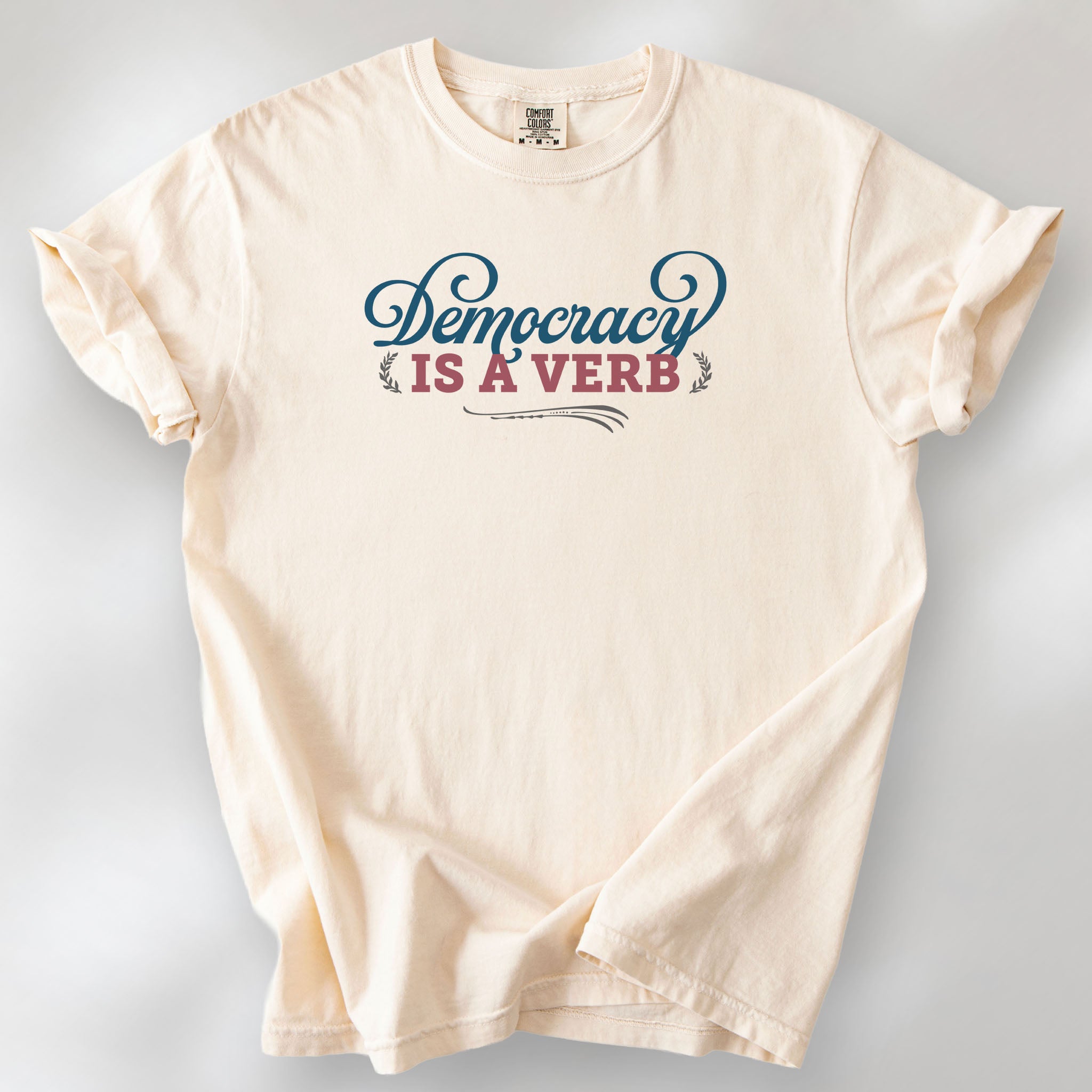 Ivory t-shirt with the phrase “Democracy Is a Verb” in decorative lettering.
