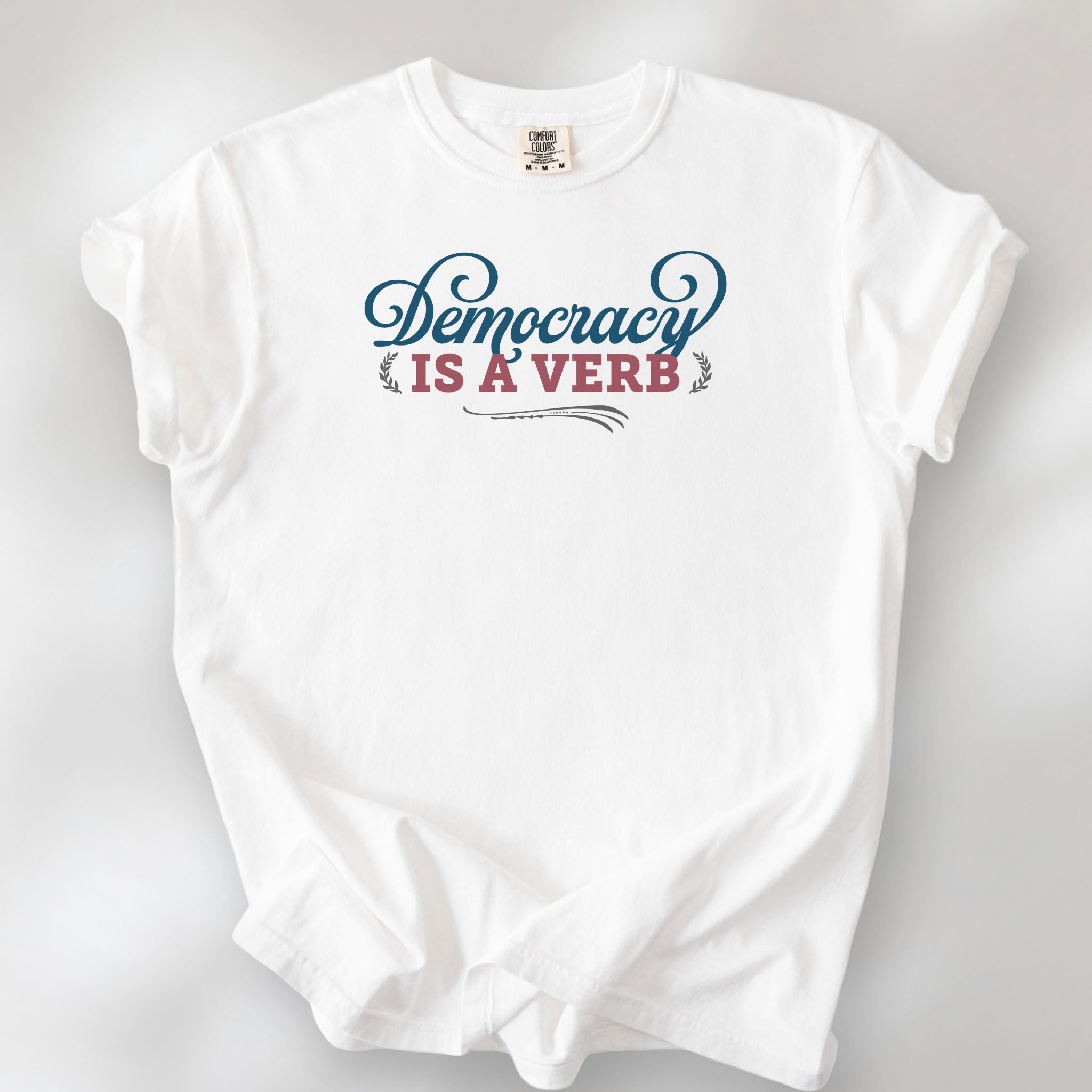 White t-shirt with the phrase “Democracy Is a Verb” in decorative lettering.