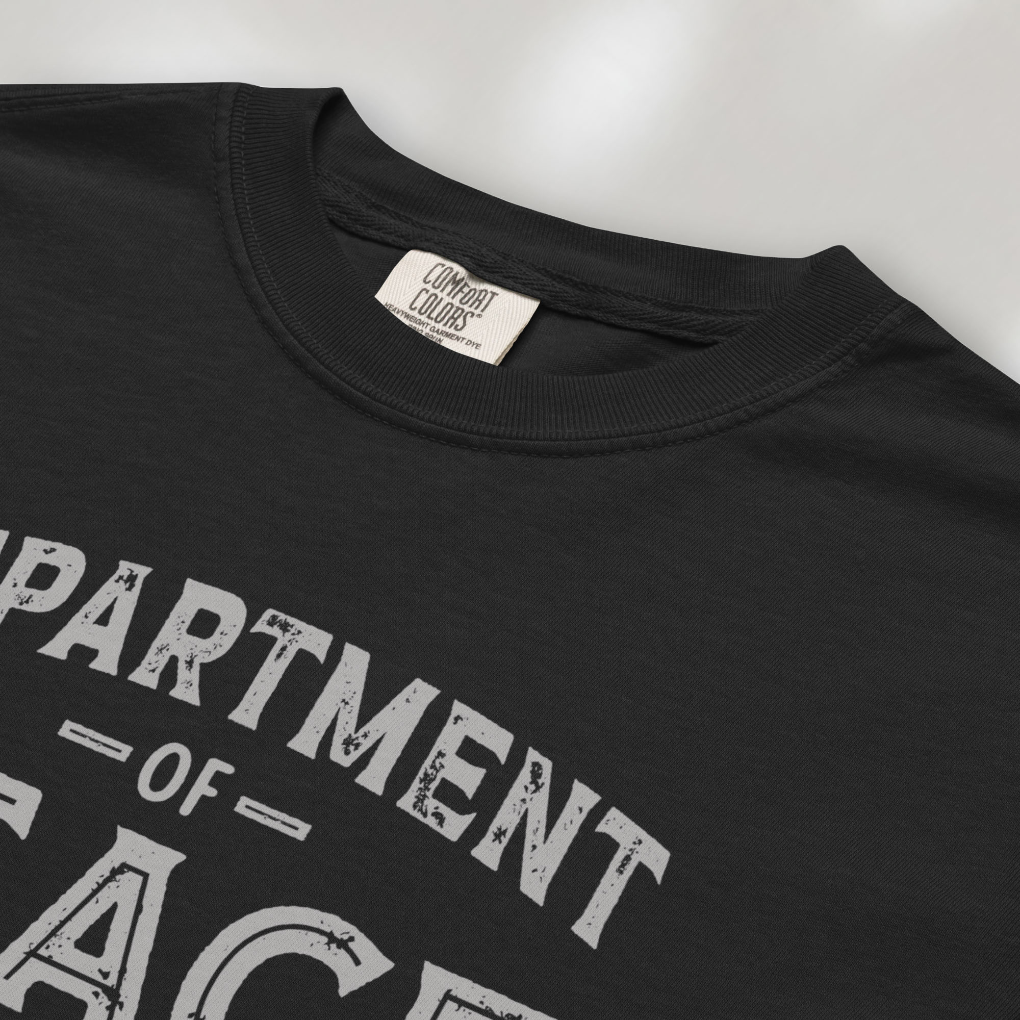 Closeup detail of black t-shirt with distressed text reading “Department of Peace — Unity is Power” in vintage style design.
